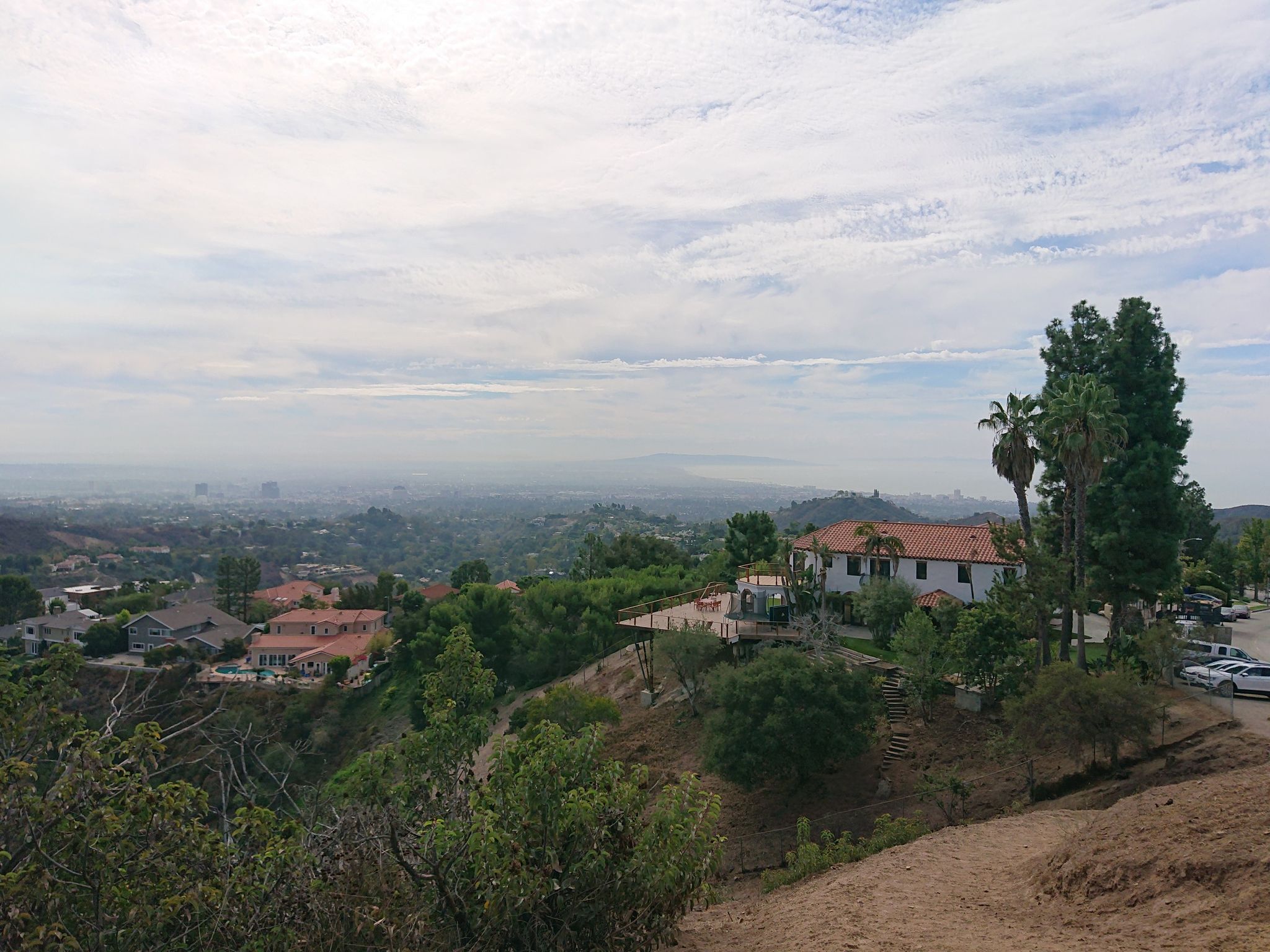 Houses on a hillside overlooking a hazy distant city under cloudy sky. - Mandeville Canyon Park loop from 17th Street/SMC