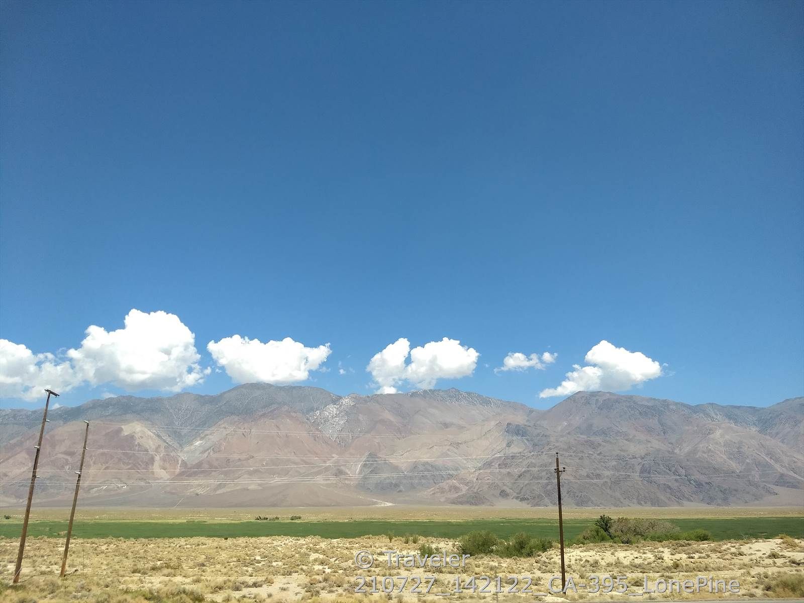 Expansive arid plain with distant mountains under a bright blue sky and white clouds. - Manzanar loop
