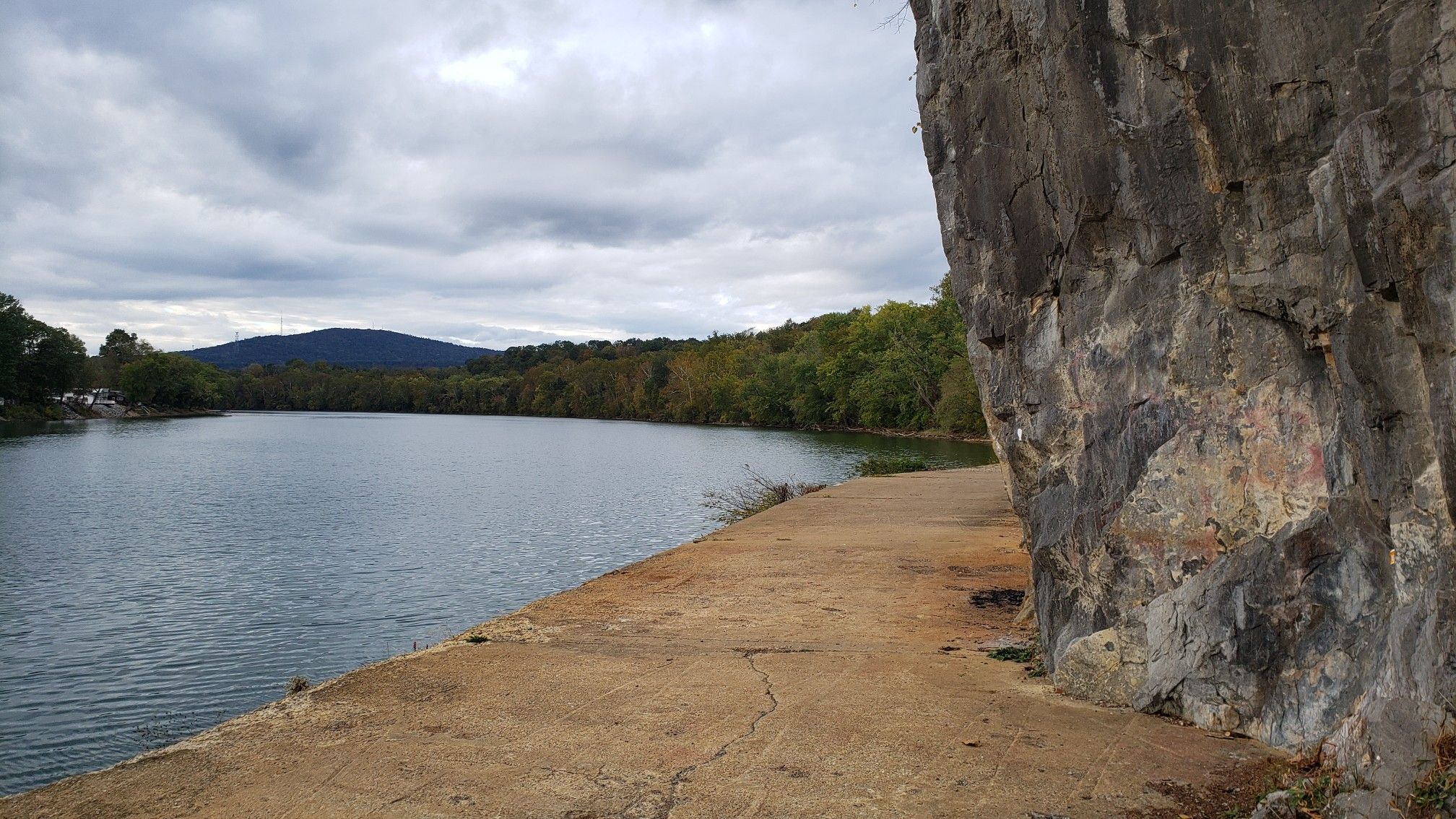 A wide river flows past a rocky cliff and forested hills under cloudy skies. - Dam Number 5 – C & O Bicycle, Hancock loop from Williamsport