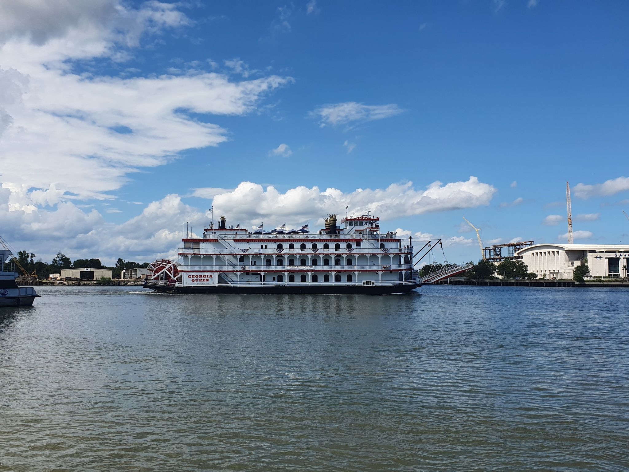 Large white paddlewheel boat on a river under a bright blue sky. - Savannah Riverfront
