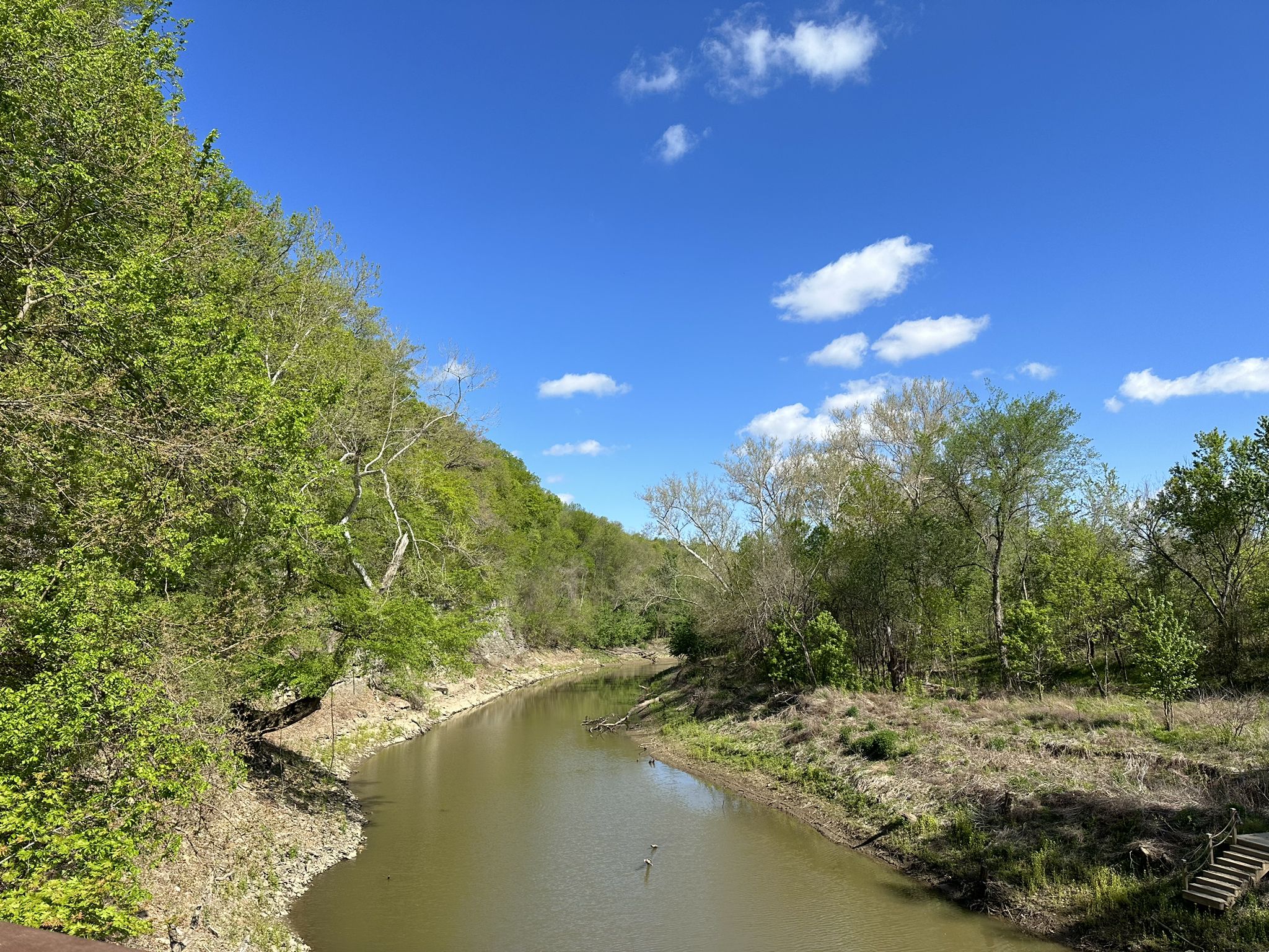 A calm river flows between lush green hills under a blue sky. - Katy Trail: Rocheport to Huntsdale
