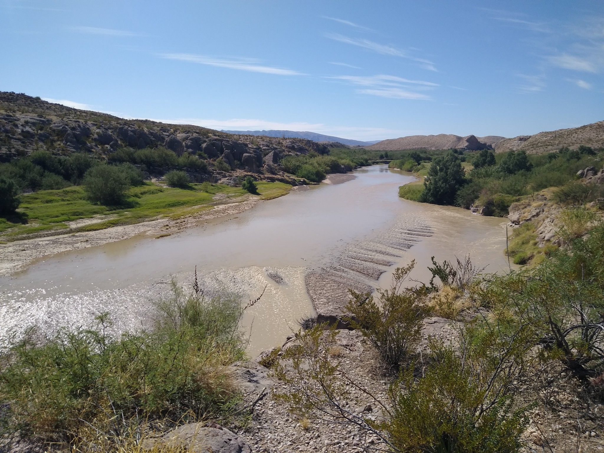 Wide, muddy river flows through a desert landscape under a bright, clear sky. - Hot Springs Historic Trail