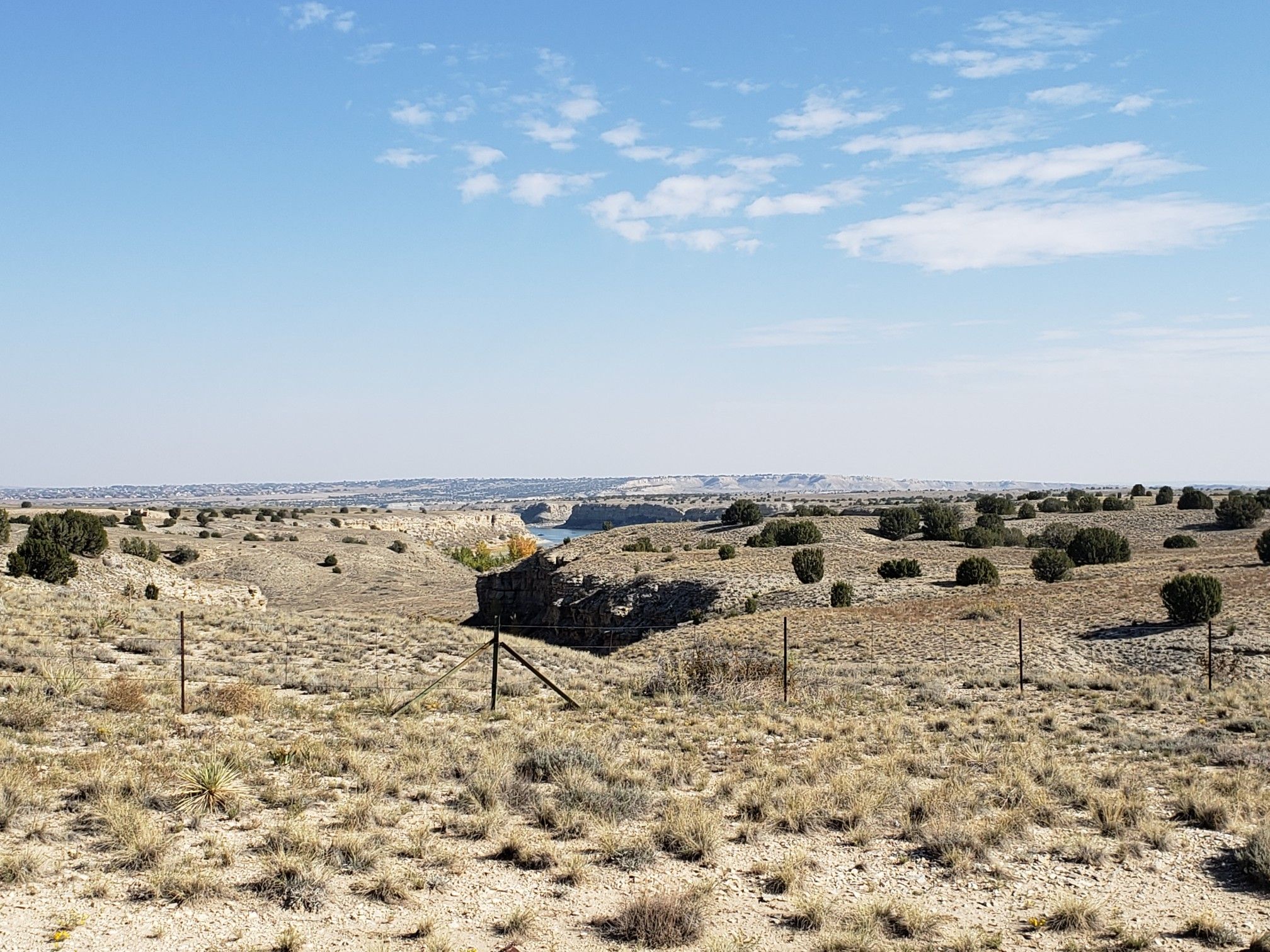 Arid landscape with sparse vegetation, fences, and a distant canyon. - Voodoo Trail loop from Pueblo Reservoir