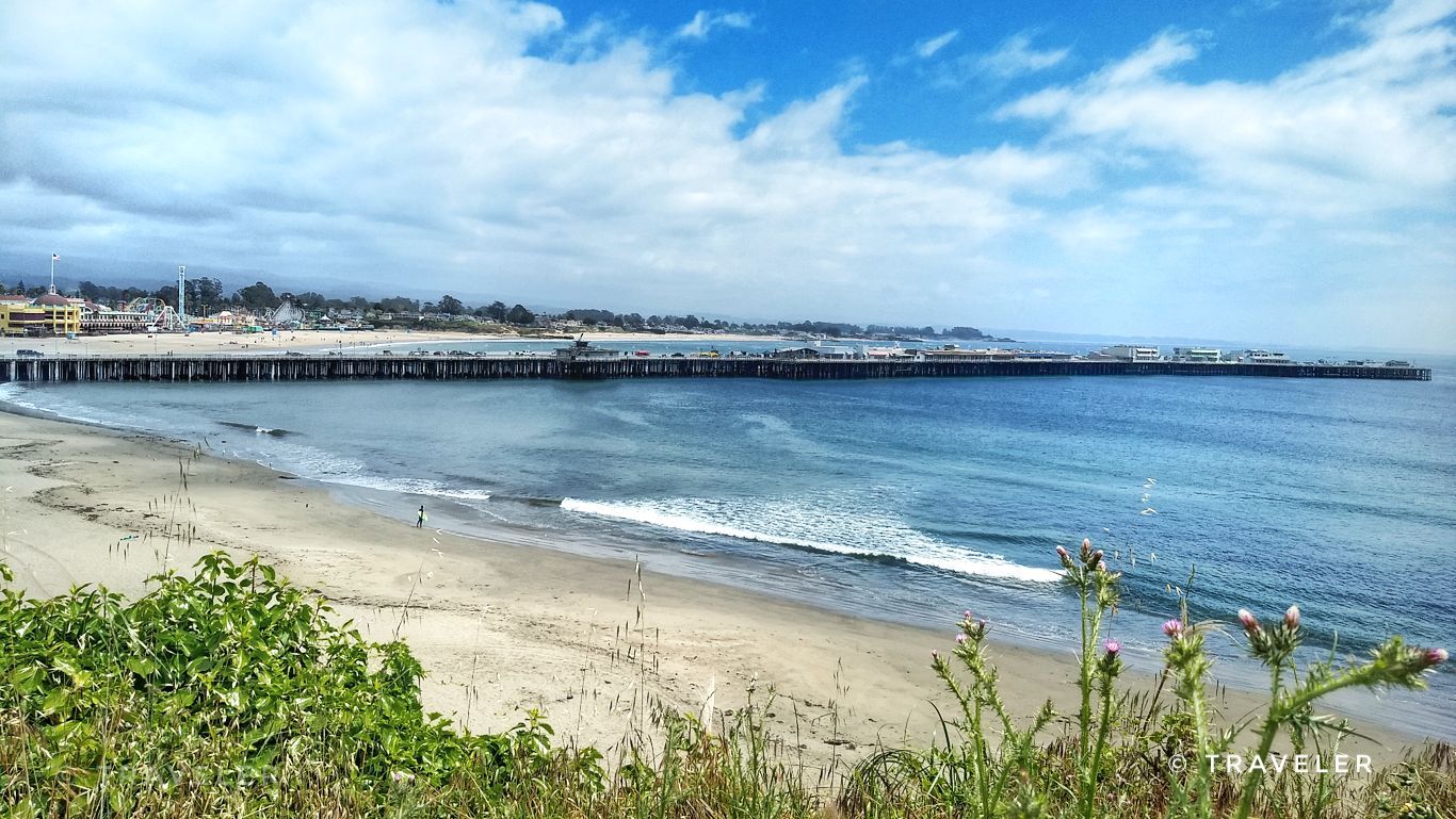 Wide sandy beach with gentle waves, a long pier, and distant buildings. - Santa Cruz West Cliff and Riverwalk Loop