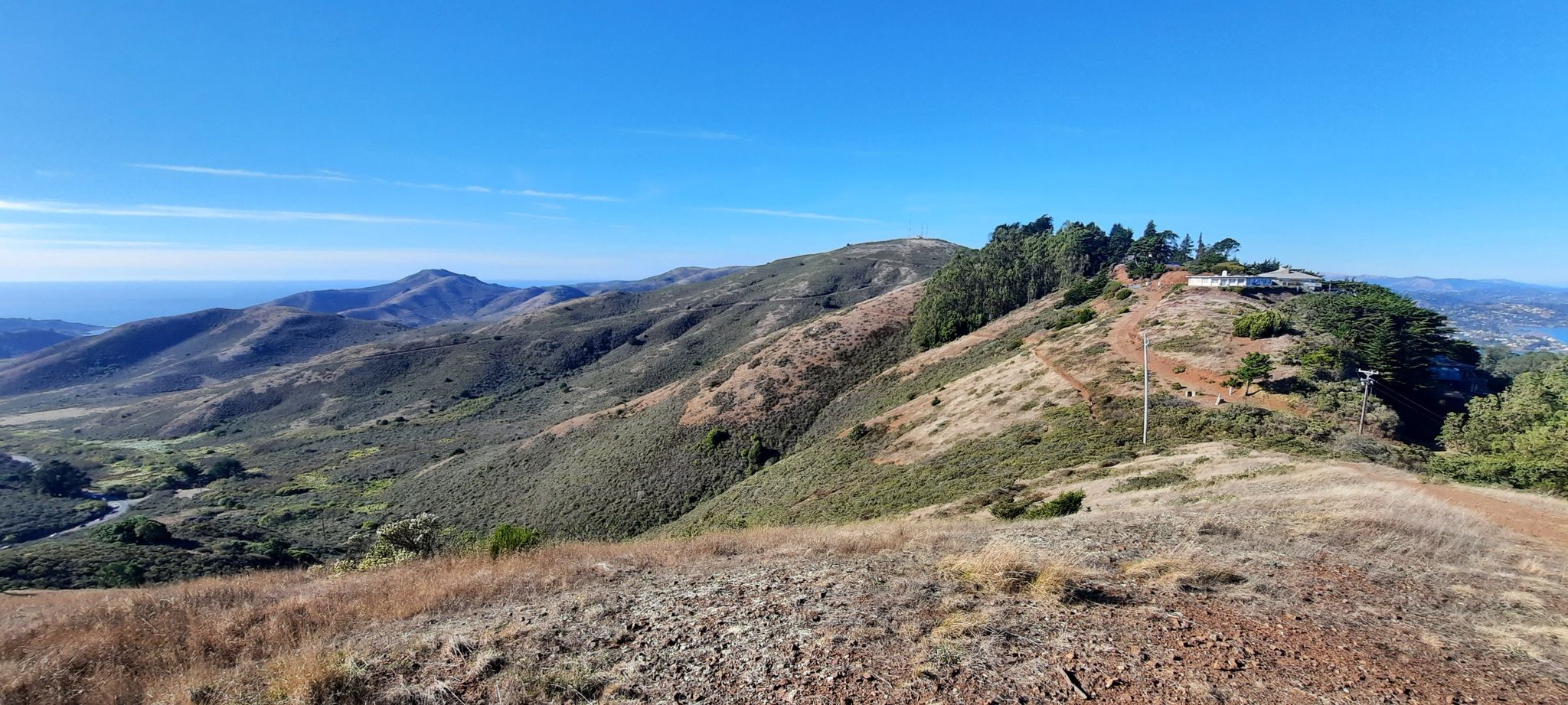 Expansive view of rolling green hills and distant ocean under blue sky. - SCA Trail to Engagement Hill