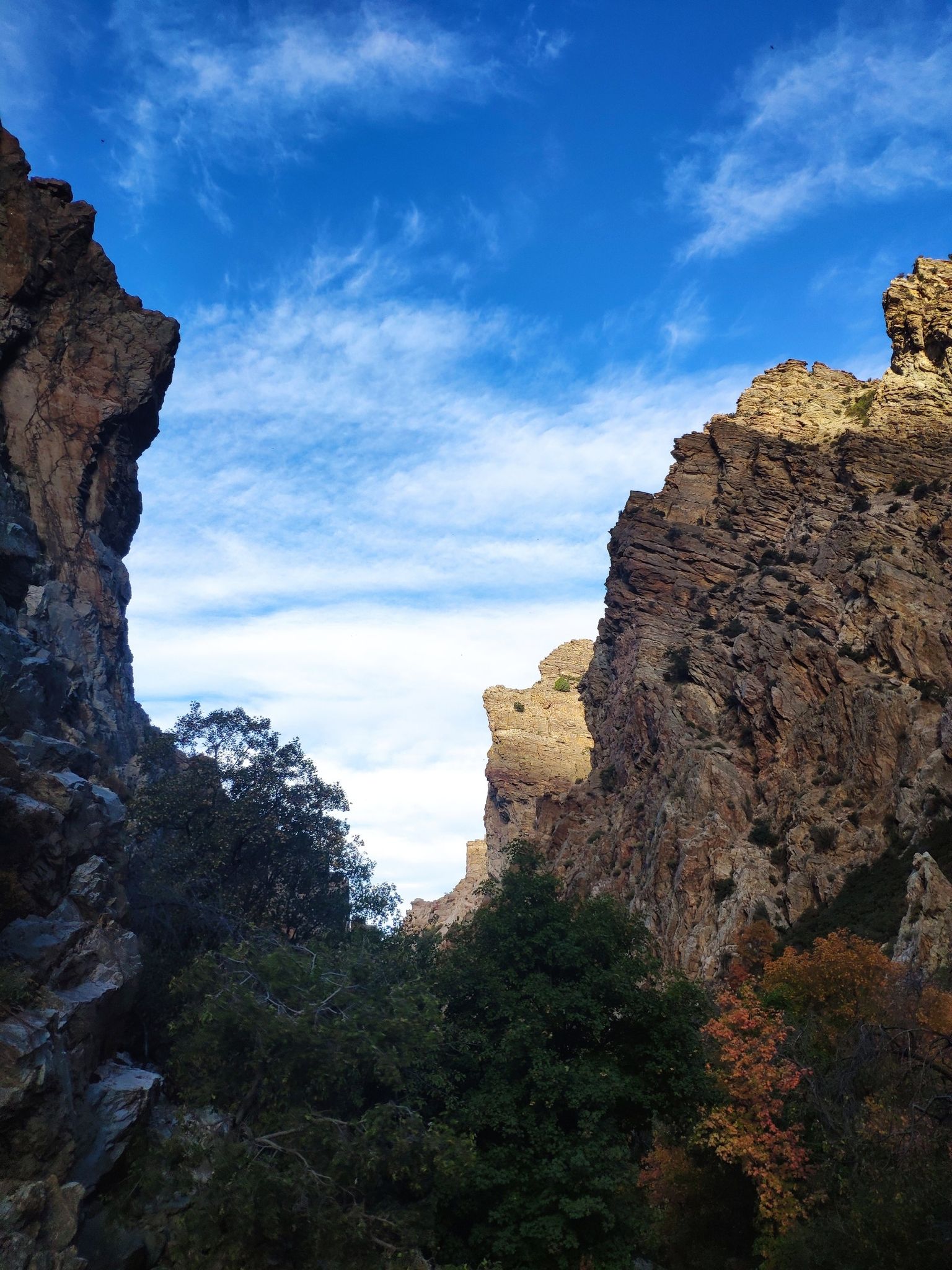 Towering rocky canyon walls frame a bright blue sky with scattered clouds. - Kyhv Peak Trail