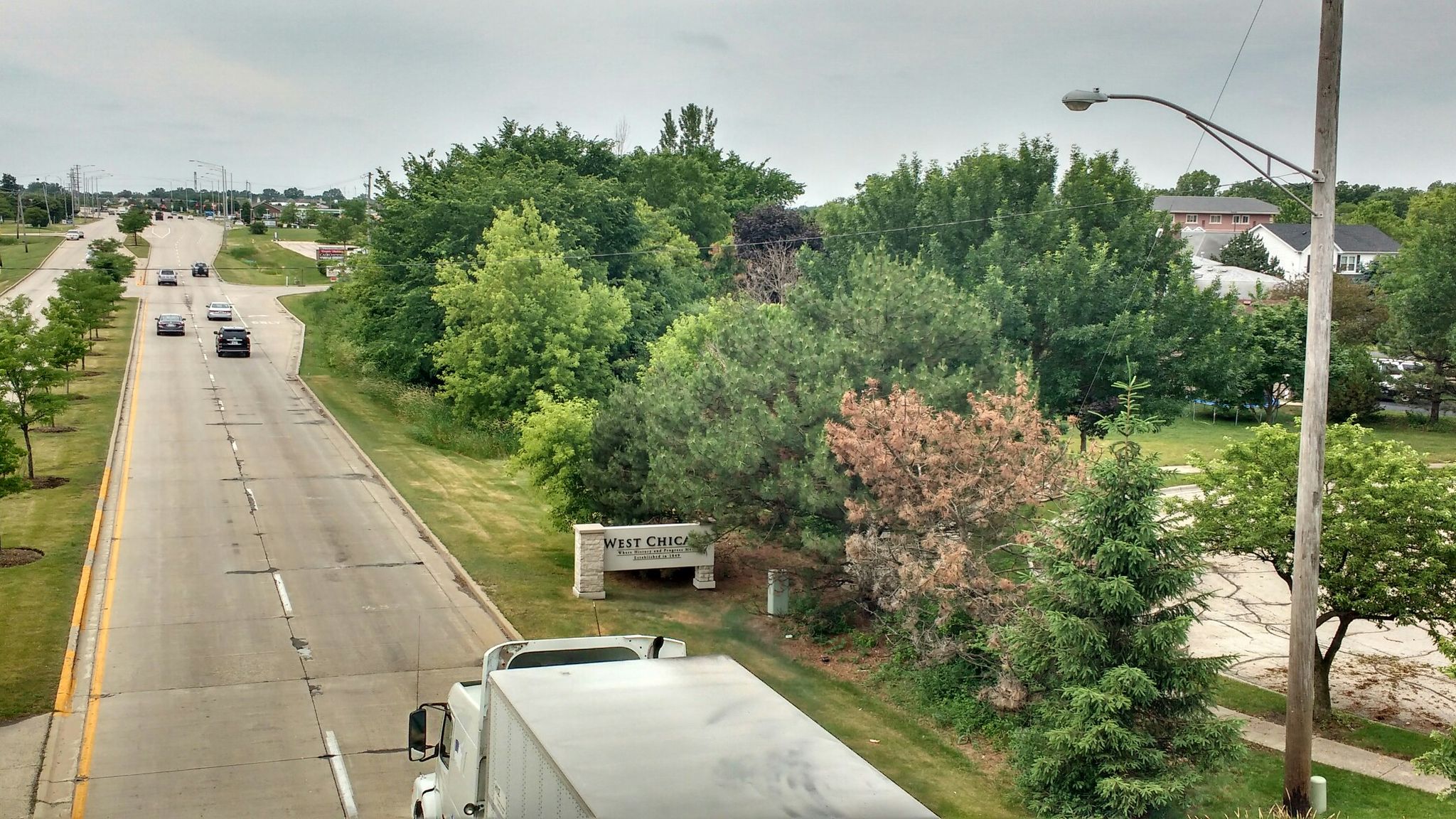 Daytime view of a road with vehicles, green trees, and houses. - Illinois Prairie Path - Elgin Branch