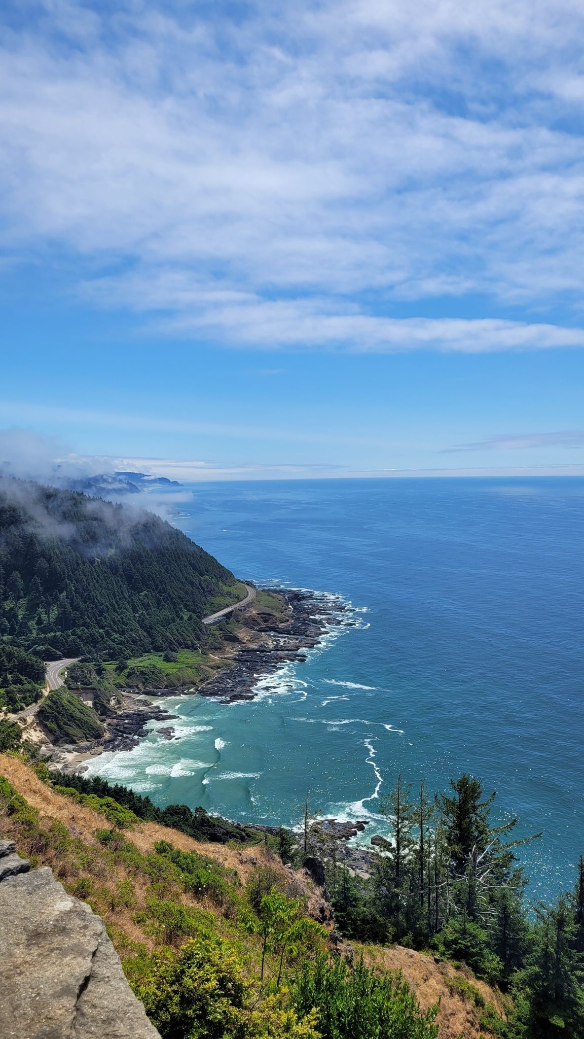 Expansive view of a rocky coastline, deep blue ocean, and winding road. - Amanda's Trail and Cape Perpetua Loop