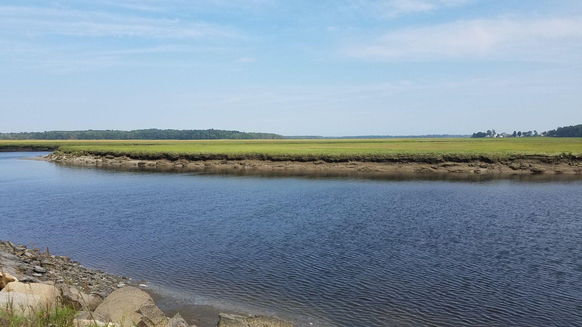 A wide river flows past green marshland under a clear blue sky. - Eastern Trail