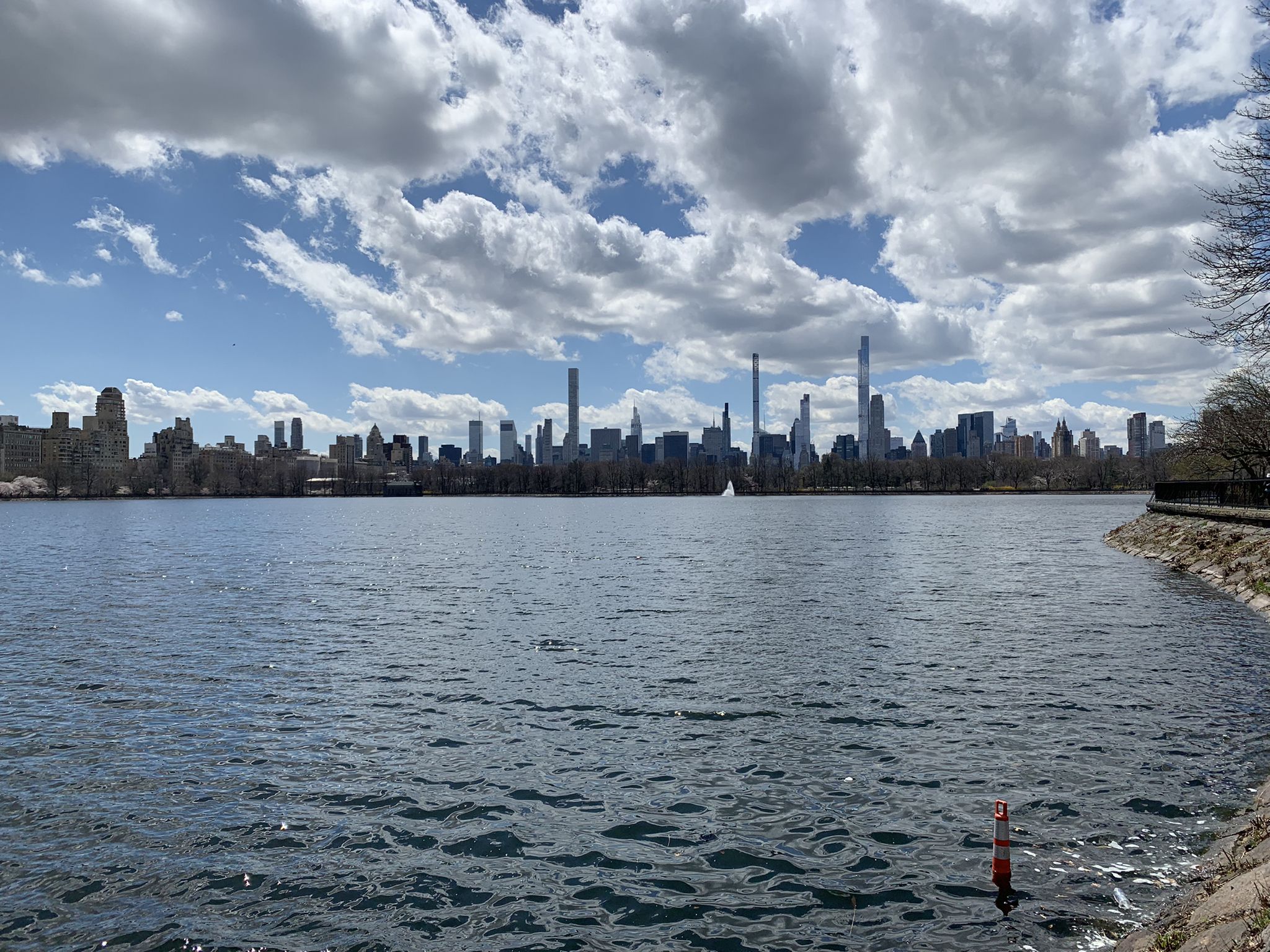 Wide lake with a distant city skyline under a partly cloudy sky. - The Pool, Central Park – Harlem Meer loop from Cathedral Parkway–110th Street
