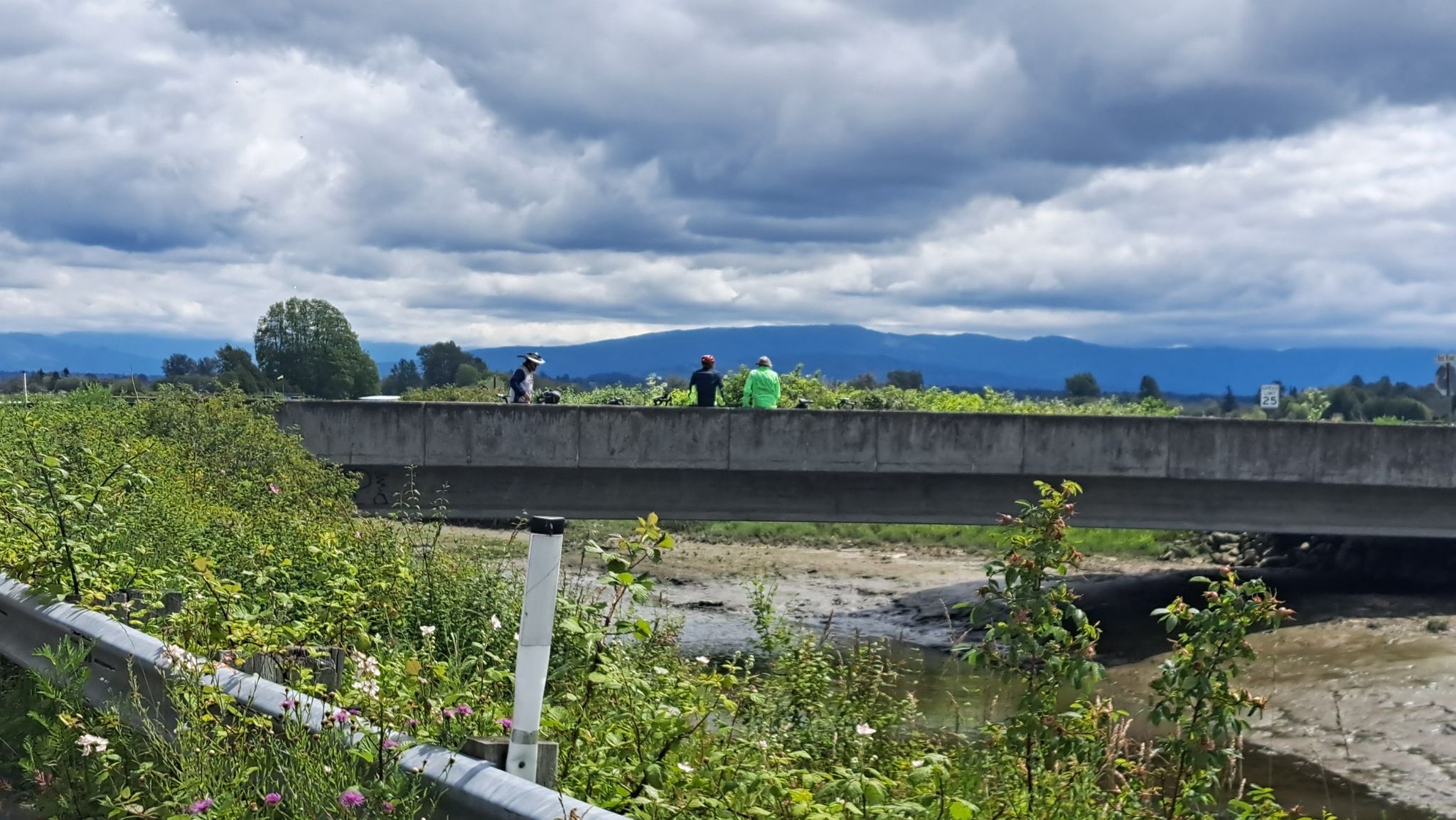 People stand on a concrete bridge over a dry riverbed, mountains in distance. - Bellingham to Birch Bay via Everson loop