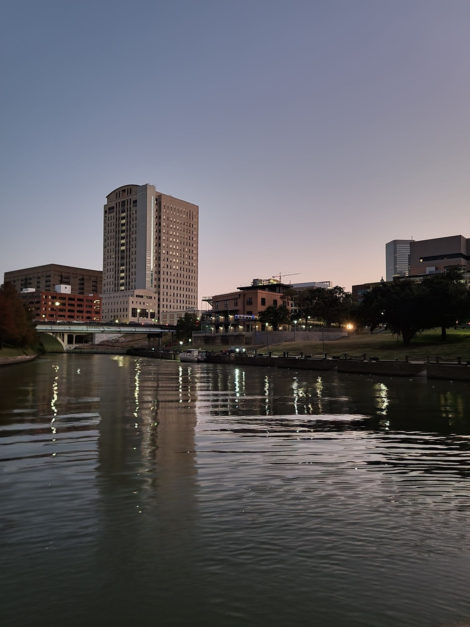 City buildings reflecting on a calm river at dusk with soft ambient light. - Lake Houston trail from Downtown