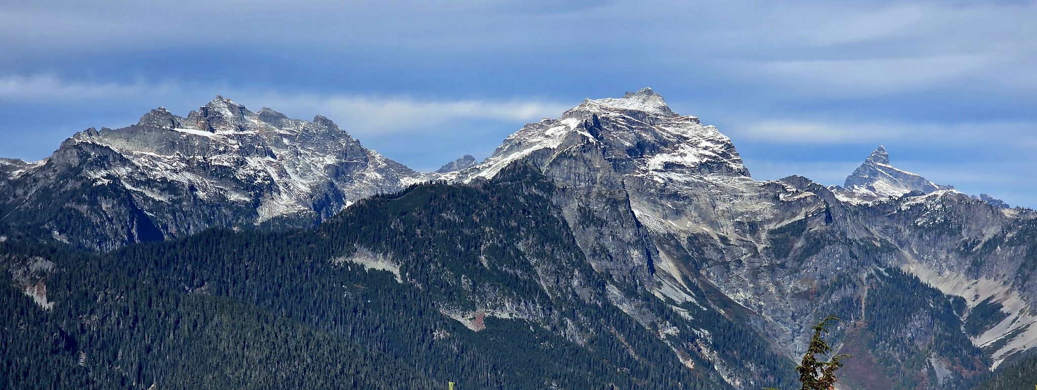 Rugged snow-capped mountains rise above a dense evergreen forest. - Frog Mountain Trail