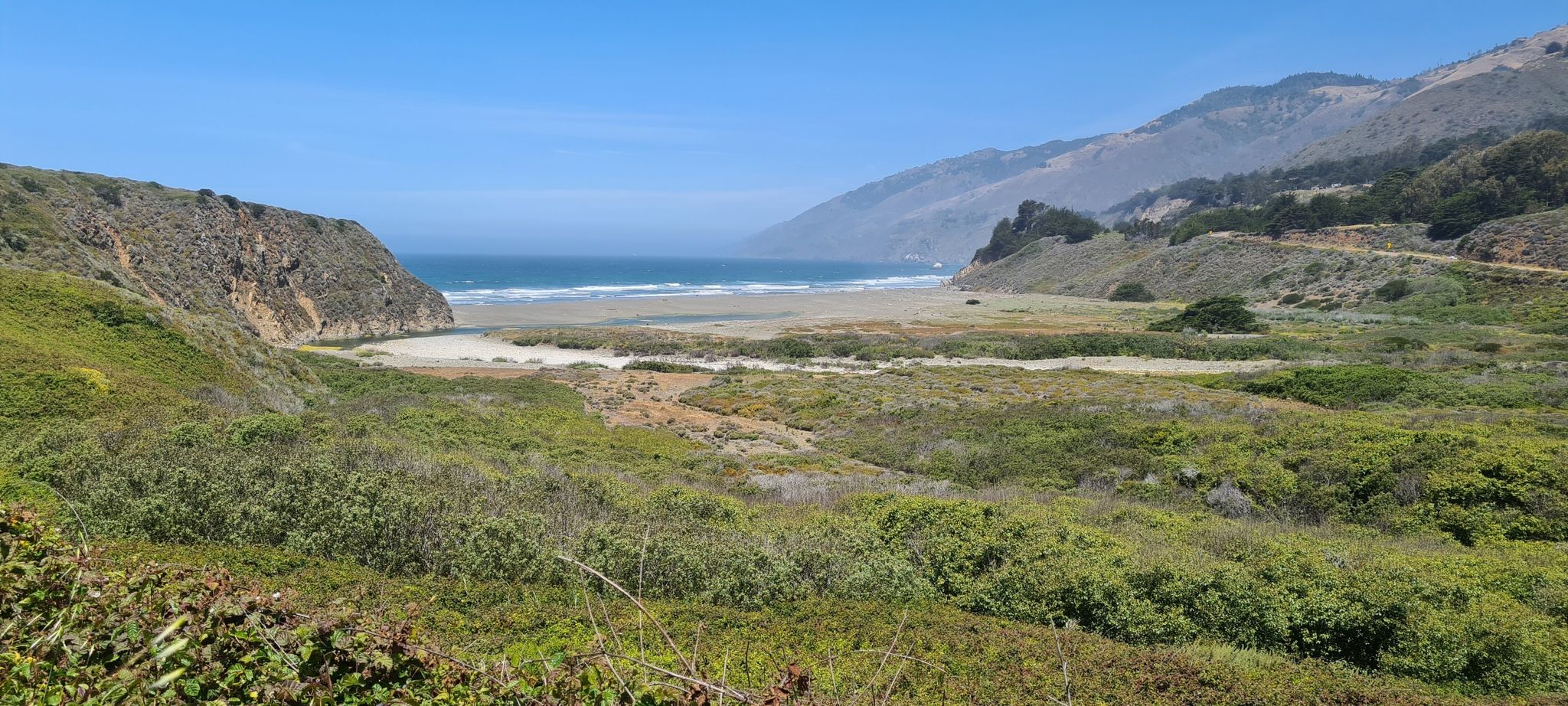 Bright coastal view of a sandy beach, ocean, and green hills. - Ragged Point via Coast Highway