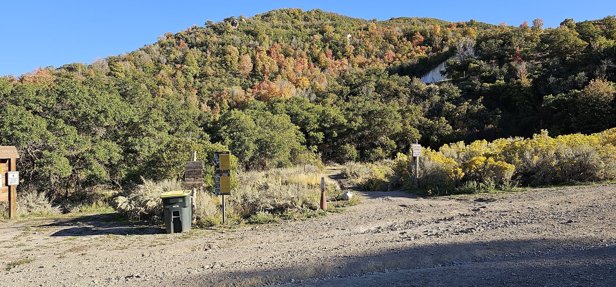 Dirt path leading to a wooded hillside with some autumn colors under bright sun. - Northwest Area Pond – Peakview Trailhead loop from Draper Utah Temple