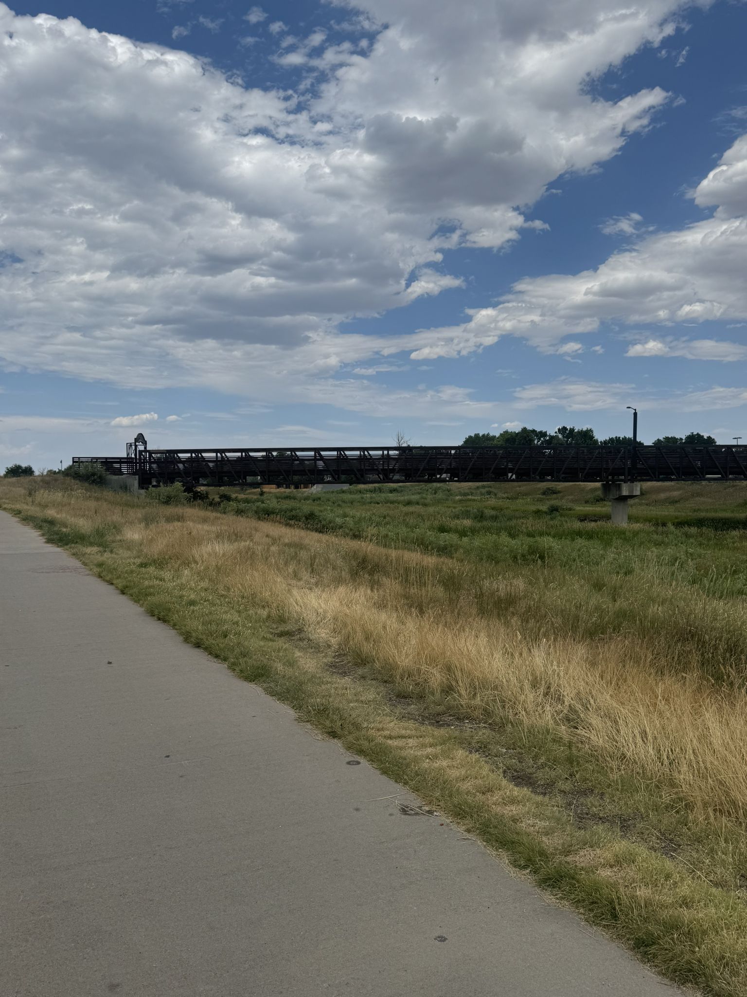 A long pedestrian bridge spans over grassy fields under a partly cloudy sky. - Denver Orbital Trail - Segment 15