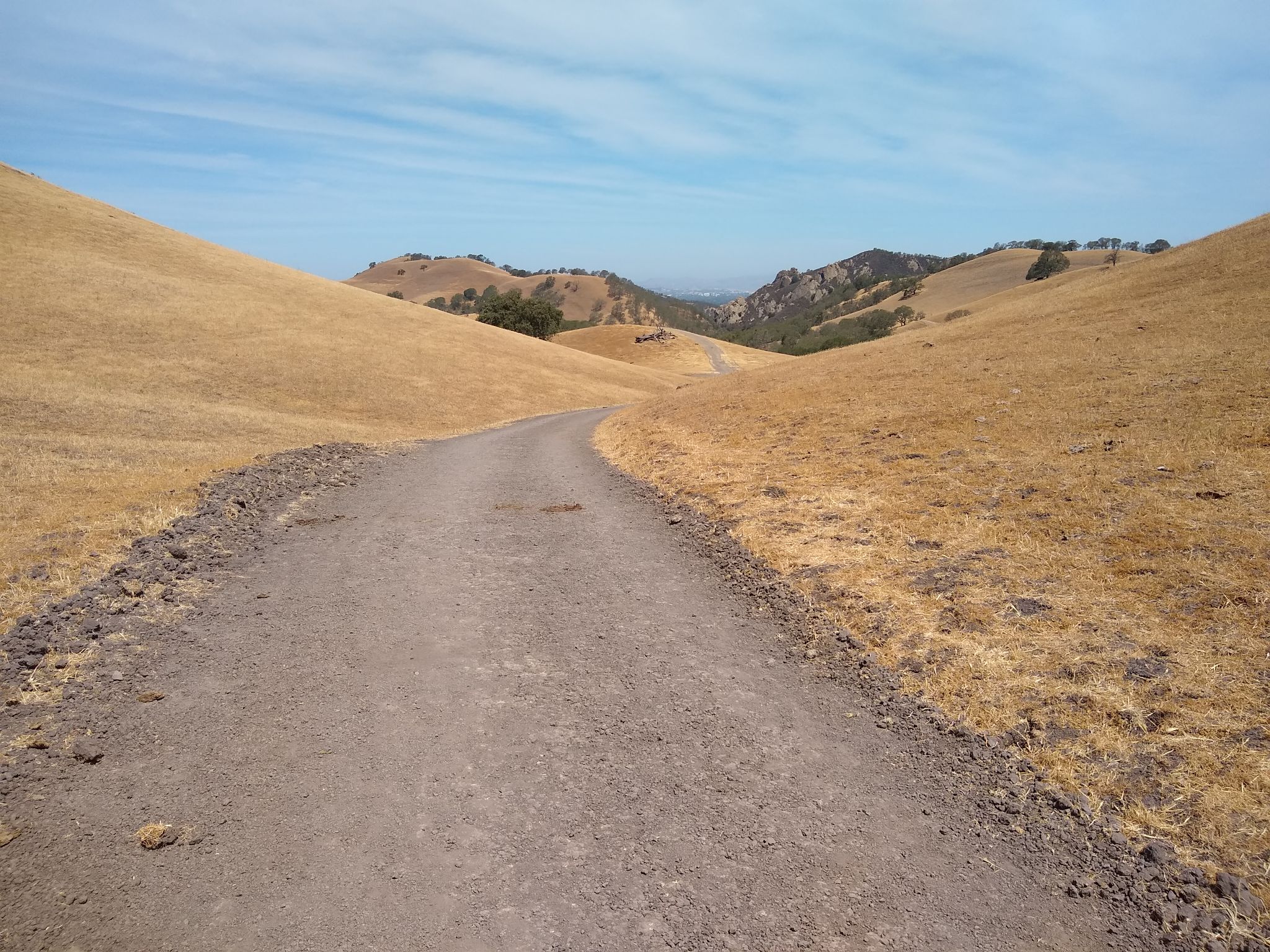 A wide dirt path cuts through golden, dry hills under a clear sky. - Stage and Wall Point Road Loop