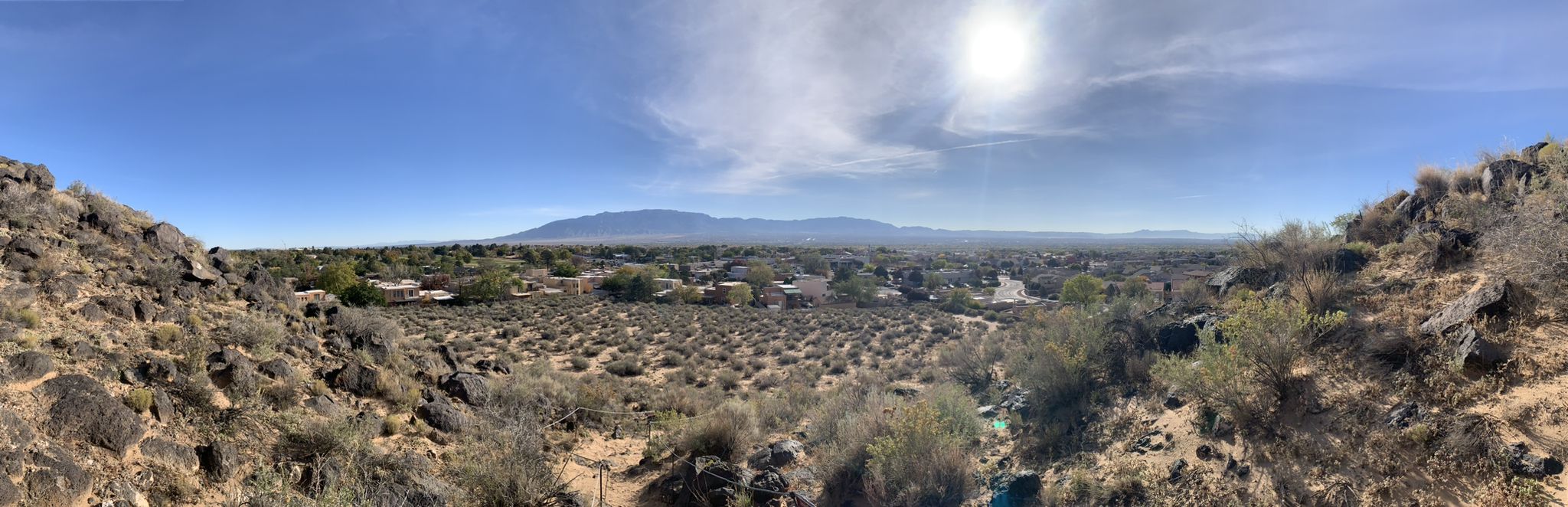 Panoramic desert landscape with distant mountains, a town, and bright sun. - Piedras Marcadas Canyon Trail