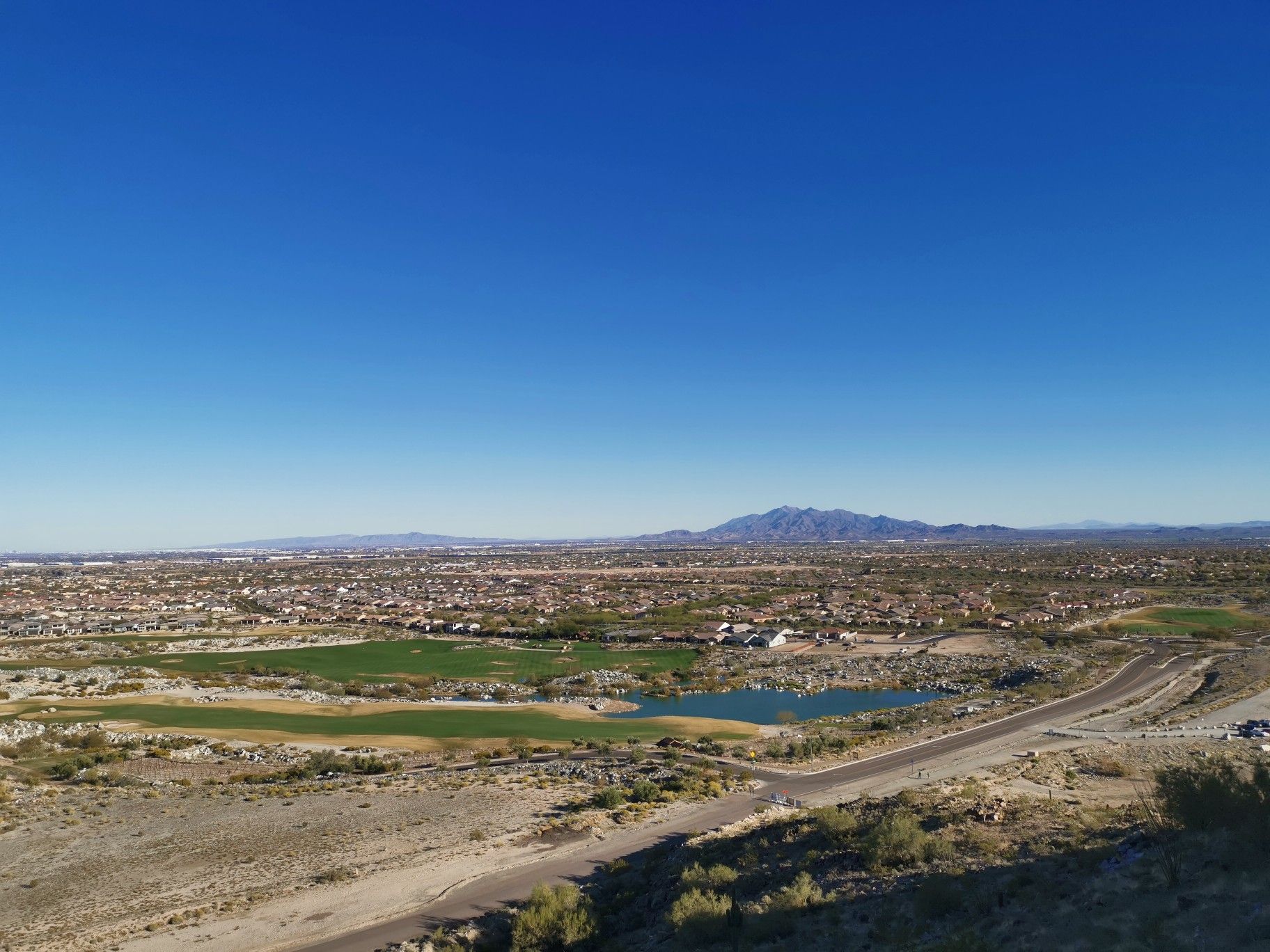 Aerial view of a desert city, golf course, and mountains under clear sky. - Verrado Mountain Loop