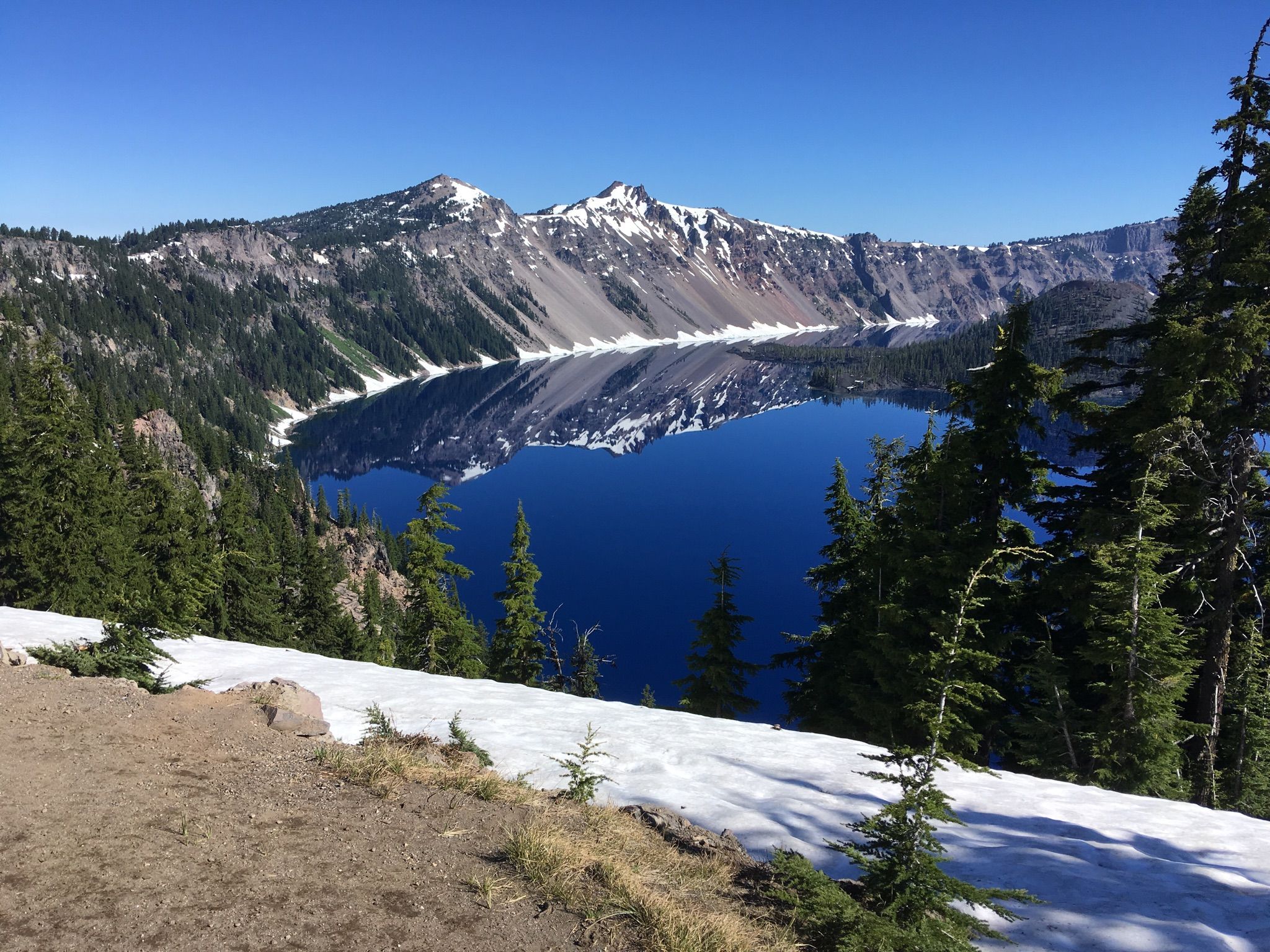 Bright blue lake reflects snow-capped mountains and pine trees under clear sky. - Dutton Creek Trail