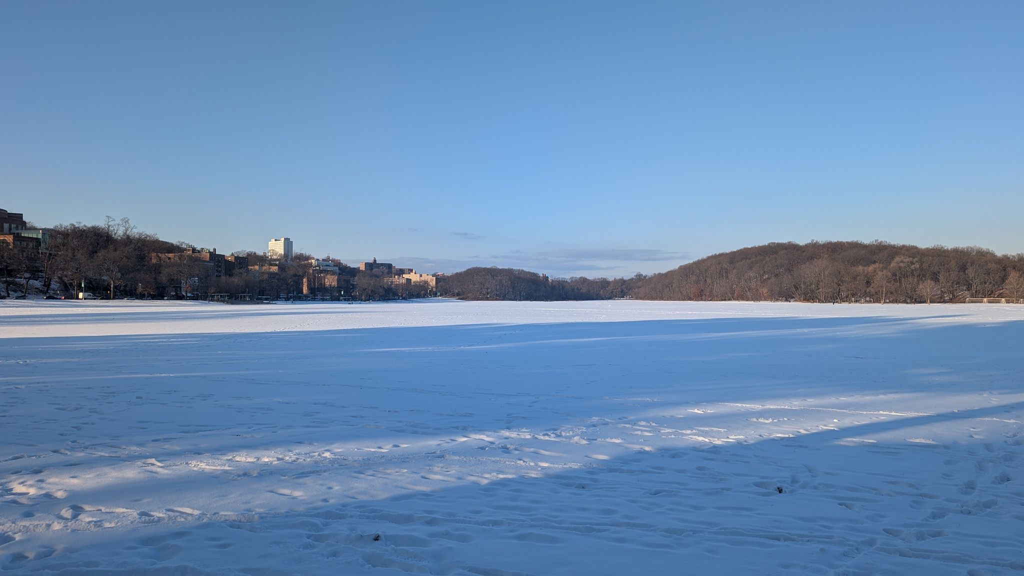 Vast snow-covered frozen lake under a clear blue sky with distant hills. - Van Cortlandt Park loop from Van Cortlandt Park