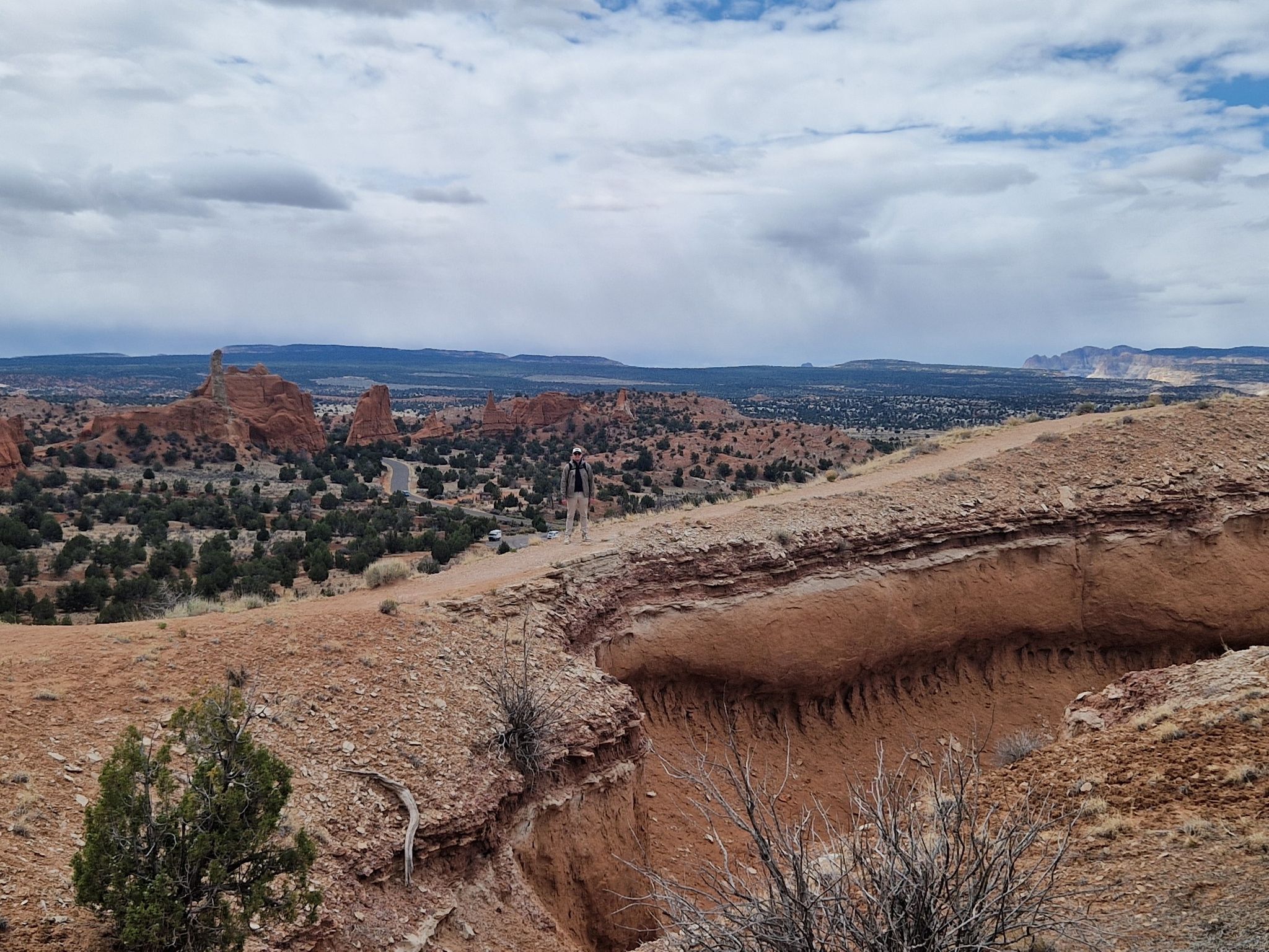 A person hiking on a dirt trail overlooking a vast desert landscape. - Angels Palace Trail