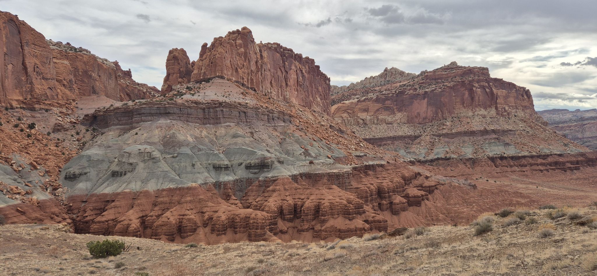 Layered red and gray rock formations dominate a desert landscape under cloudy skies. - Chimney Rock Loop Trail
