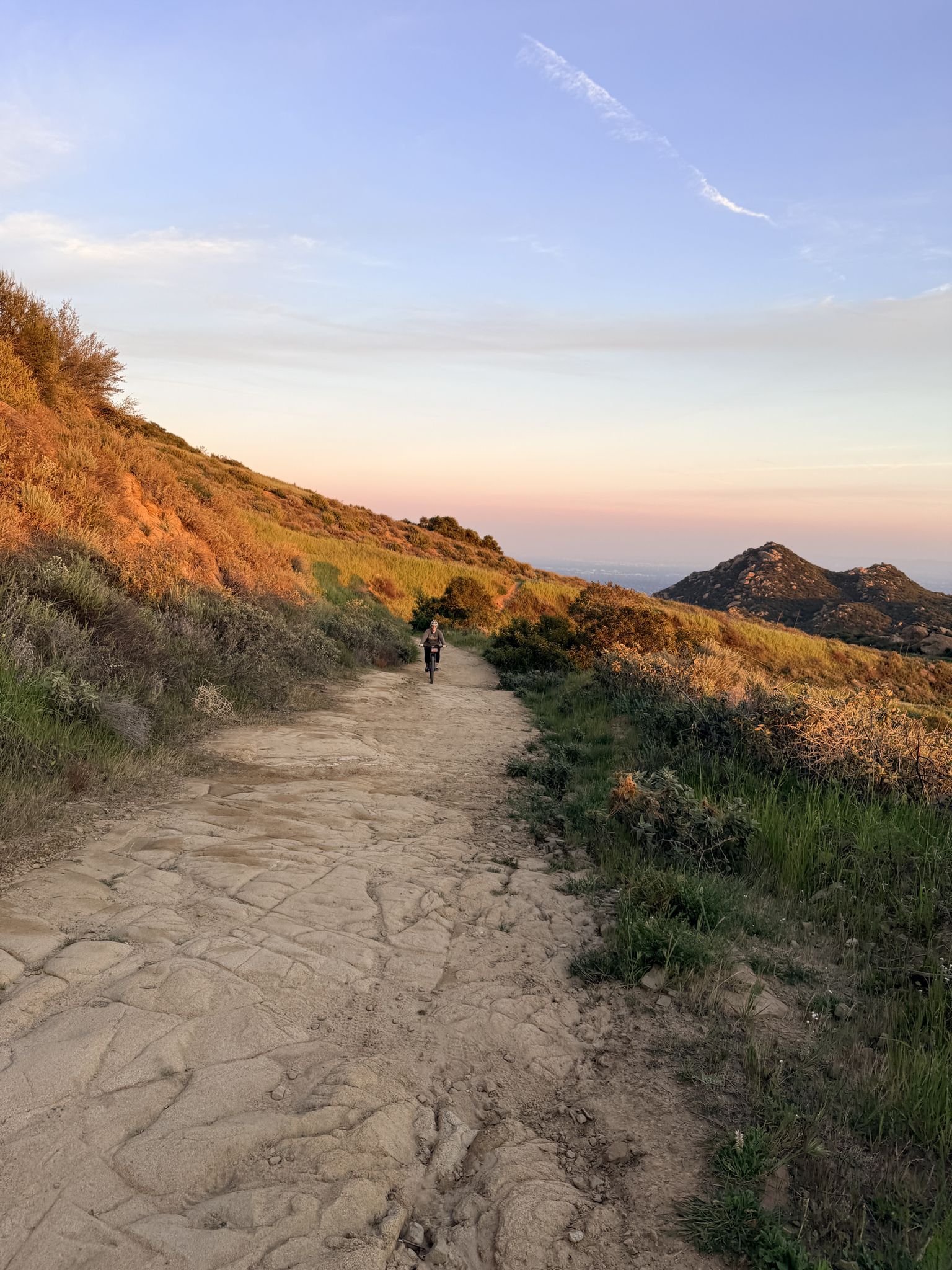 Dirt path at sunset with warm light on hills and a distant person. - Corriganville Park Picnic Area – Rocky Peak Trail loop from Santa Susana