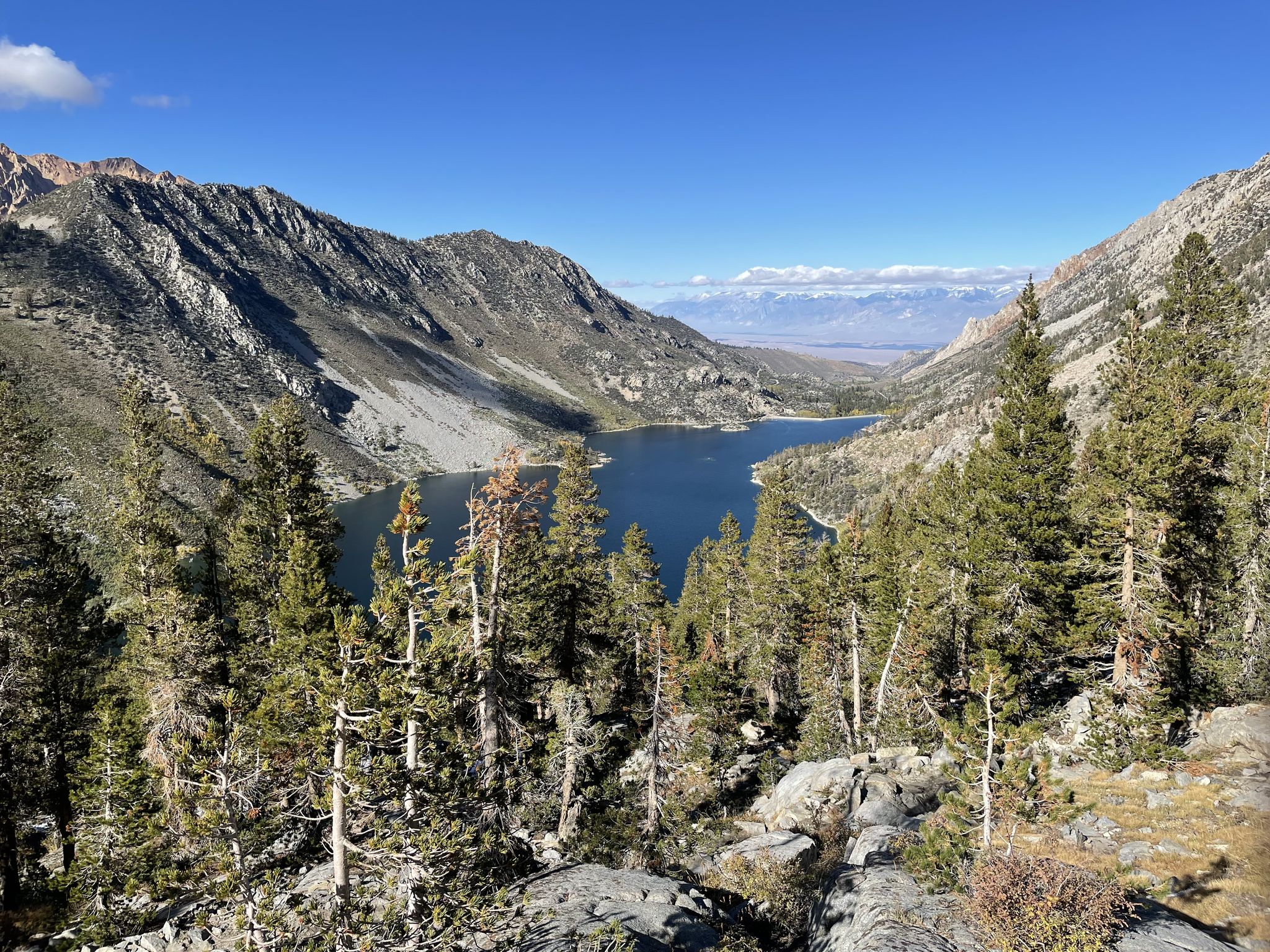 Elevated view of a large blue lake surrounded by pine forests and distant mountains. - Sabrina Basin Trail
