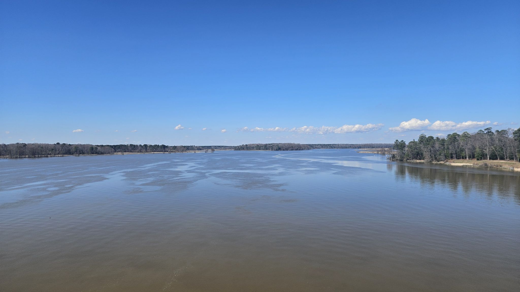Expansive calm river reflecting a clear blue sky, with distant tree lines. - Virginia Capital Trail
