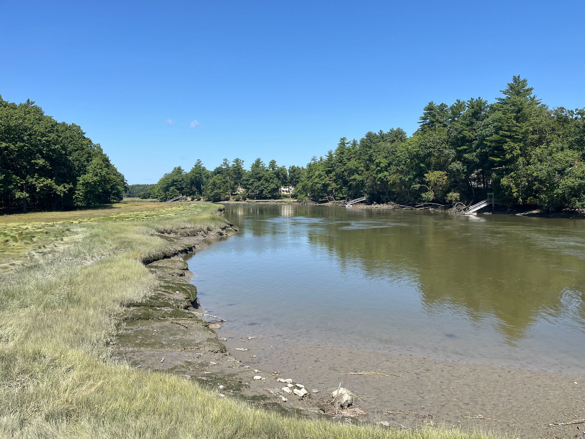 Calm river with grassy banks, dense trees, and distant docks under a clear sky. - East Coast Greenway via Cider Hill Road loop