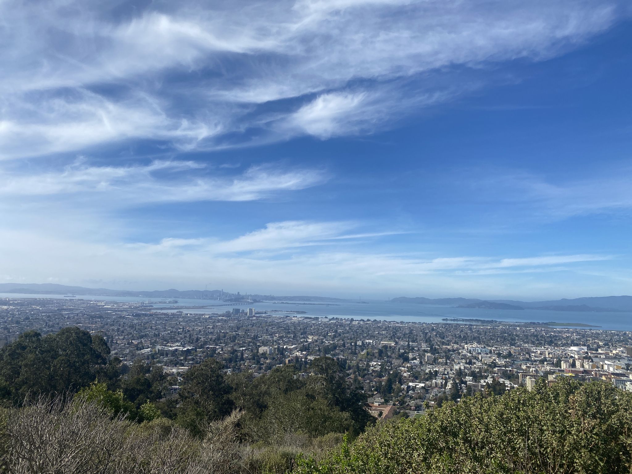 Wide view of a city and bay under a bright, wispy blue sky. - Golden Gate Bridge View – San Francisco View loop from California Memorial Stadium