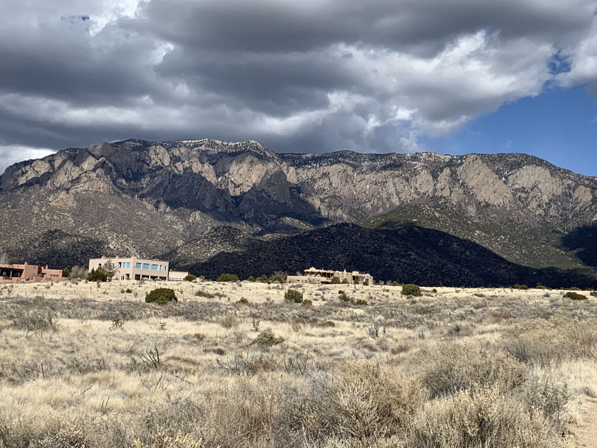 Large mountain range under dramatic cloudy sky, dry landscape with buildings. - Intersection of Trails 365 and 366 – Foothills Trail North loop from Prince of Peace Catholic Community