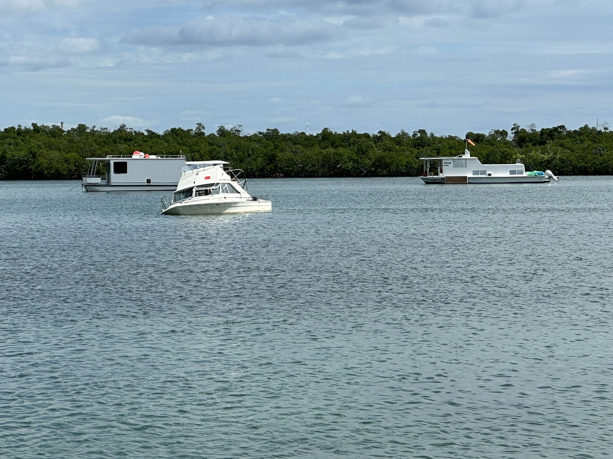 Three boats floating on calm water, with a lush green shoreline behind. - Key West International Airport loop from Stock Island