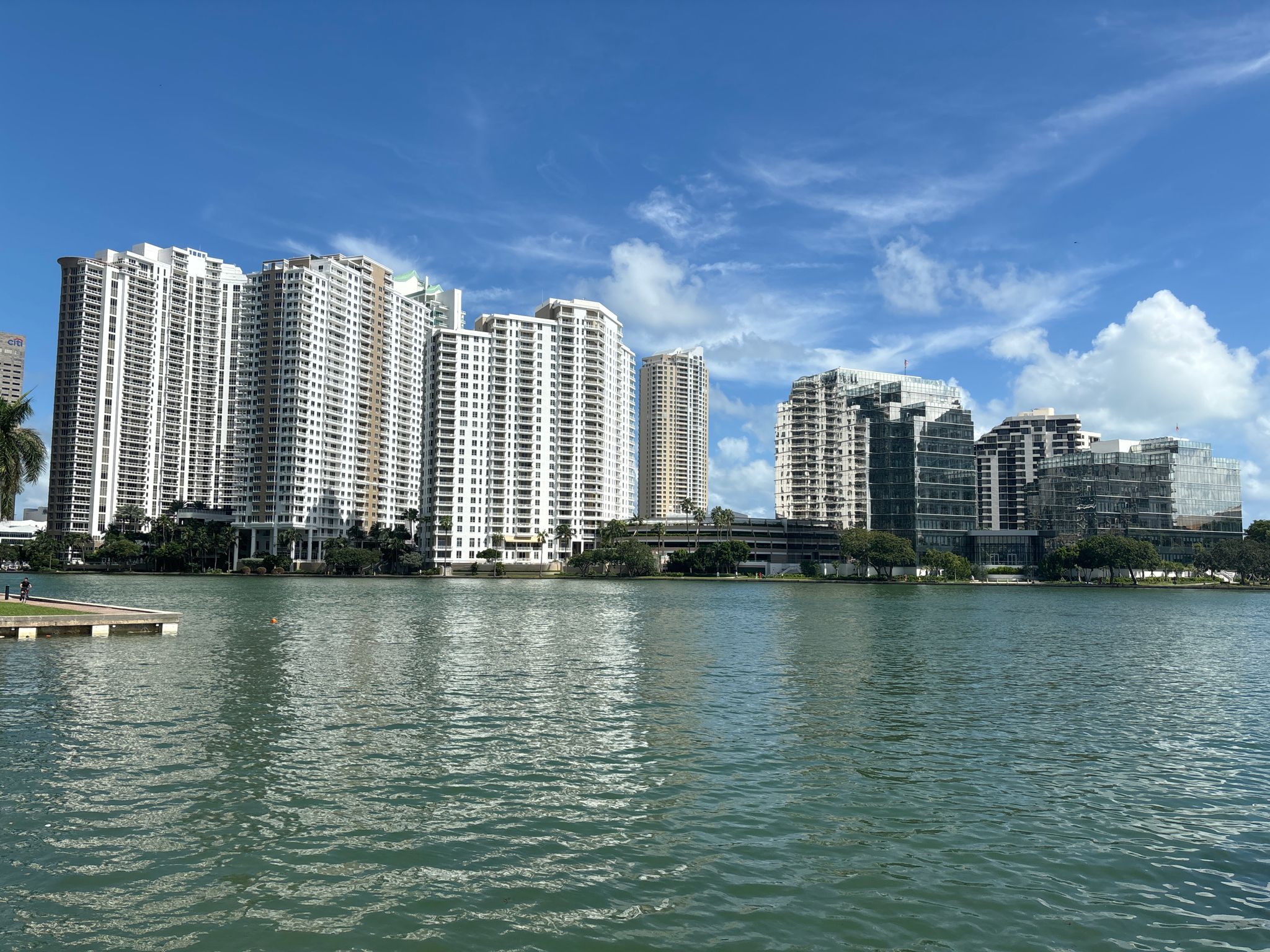 City skyline with many tall buildings along a wide waterway under a blue sky. - Brickell Key Loop