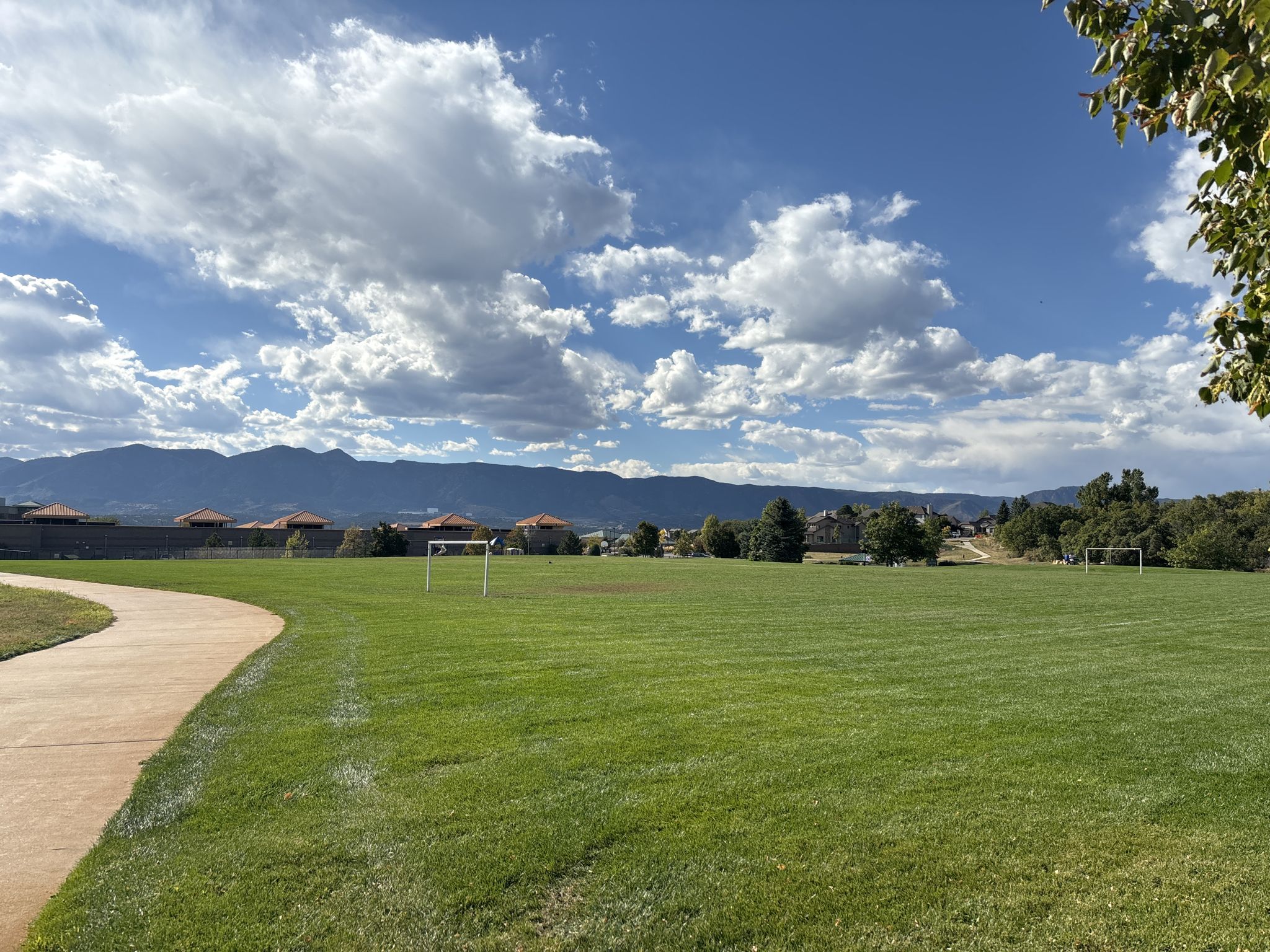 Expansive green sports field with soccer goals, path, and distant mountains under blue sky. - Mary Kyer Park loop from New Life Church