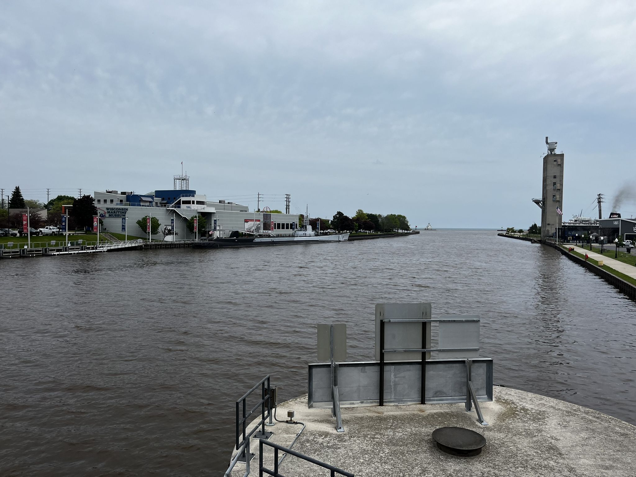 Wide river with buildings and a tall tower under an overcast sky. - Mariners Trail