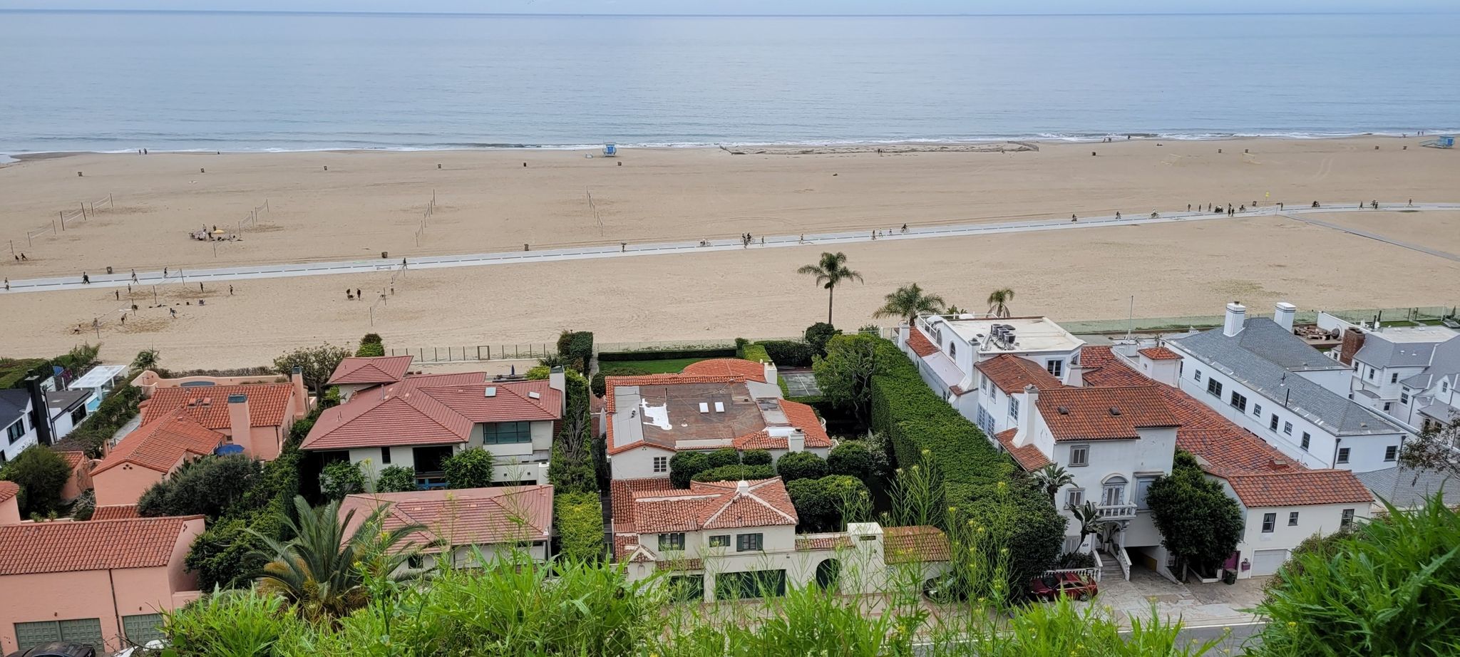 Aerial view of houses, wide sandy beach, ocean, and people under bright sky. - Santa Monica Bluffs Trail