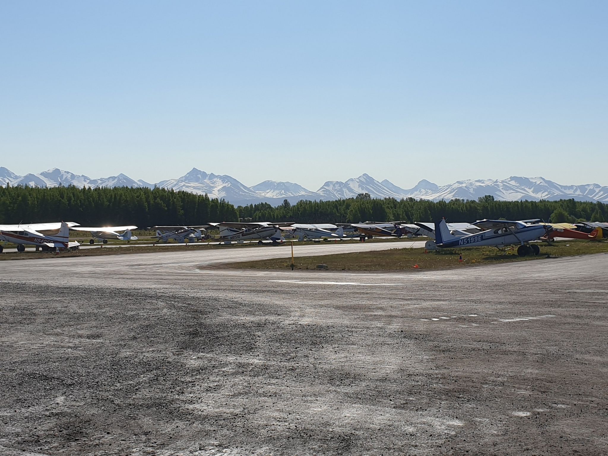Small planes parked on an airfield with distant snow-capped mountains under clear skies. - Lake Hood and Lake Spenard loop