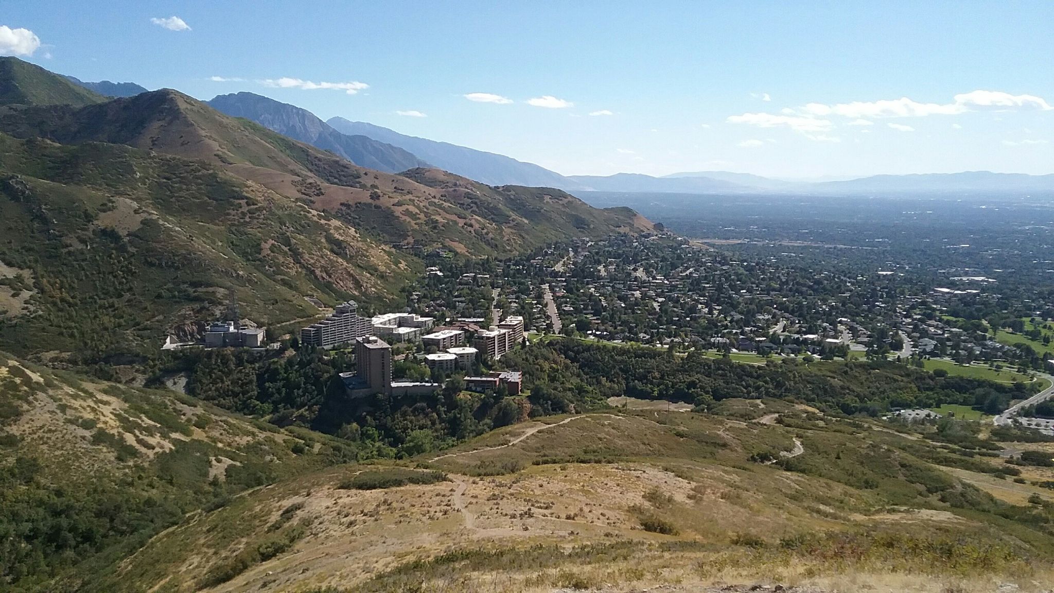 Sunny panoramic view of a city nestled in a valley surrounded by mountains. - This Is the Place Monument – Mount Wire loop from This is the Place Monument