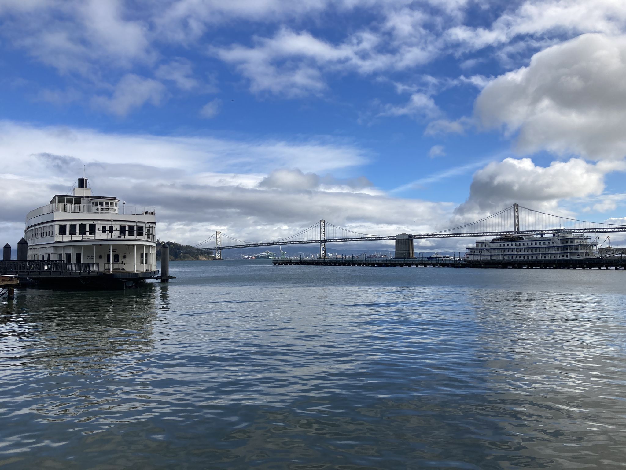 Large white ferry and suspension bridge over water under blue sky. - San Francisco Bay Trail