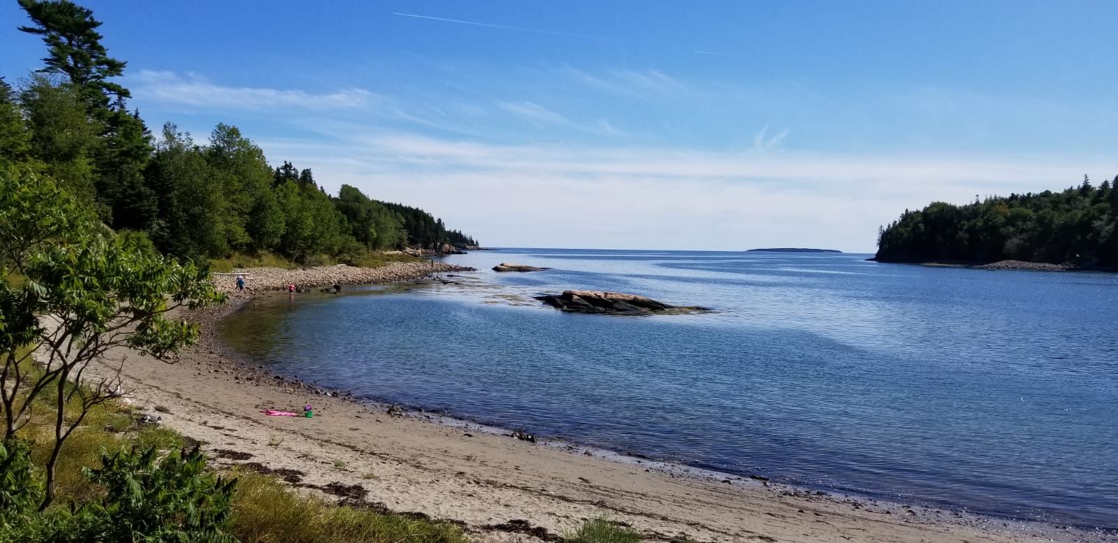Sunny coastal inlet with sandy beach, calm blue water, and distant trees. - Thunder Hole – Otter Cliffs loop from Ox Hill