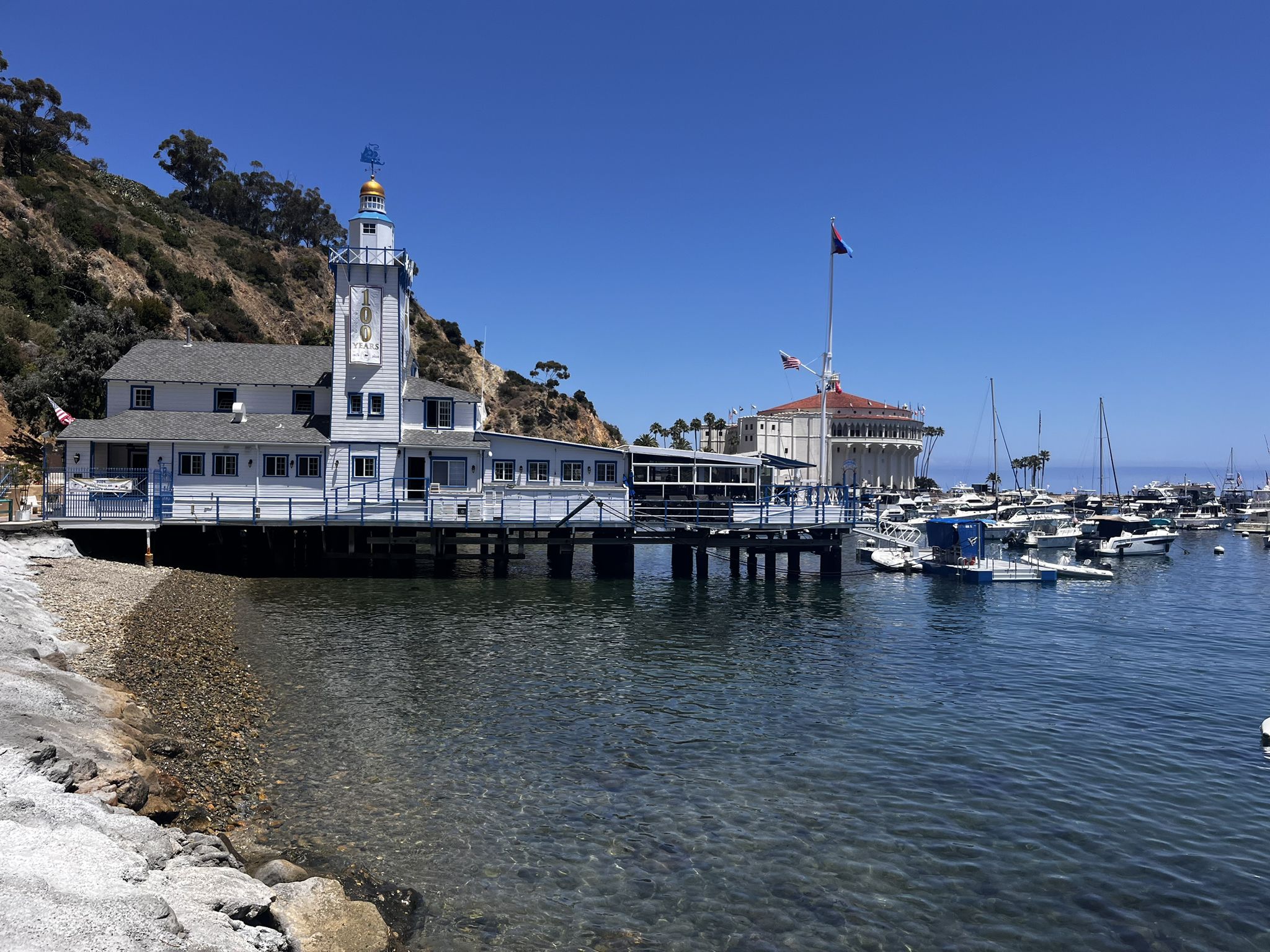 White building with lighthouse tower on pier, boats in sunny harbor. - Avalon Bay Trail
