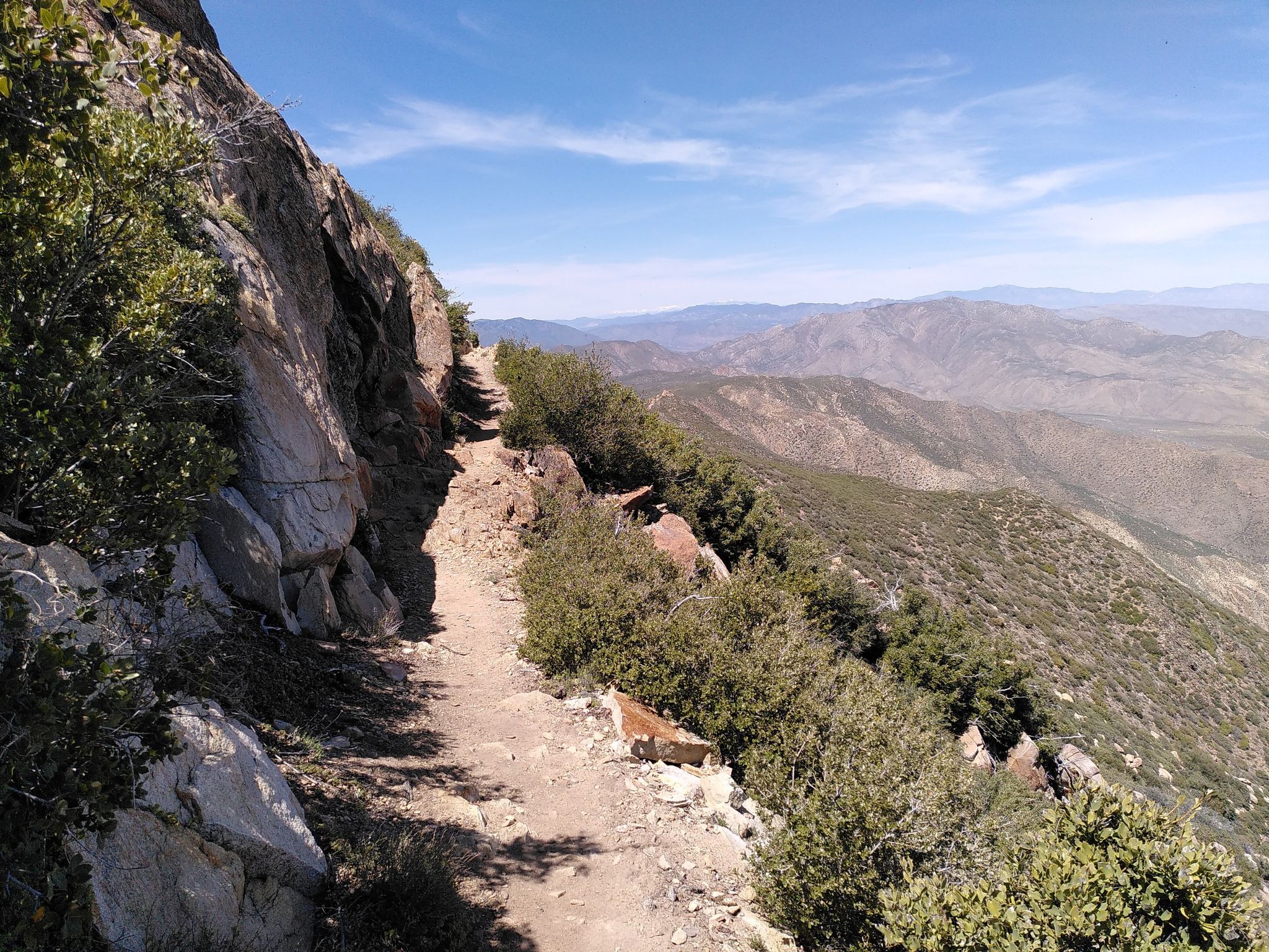 Mountain trail alongside a rocky cliff with distant hills under a blue sky. - Laguna Mountain Ridge via the PCT