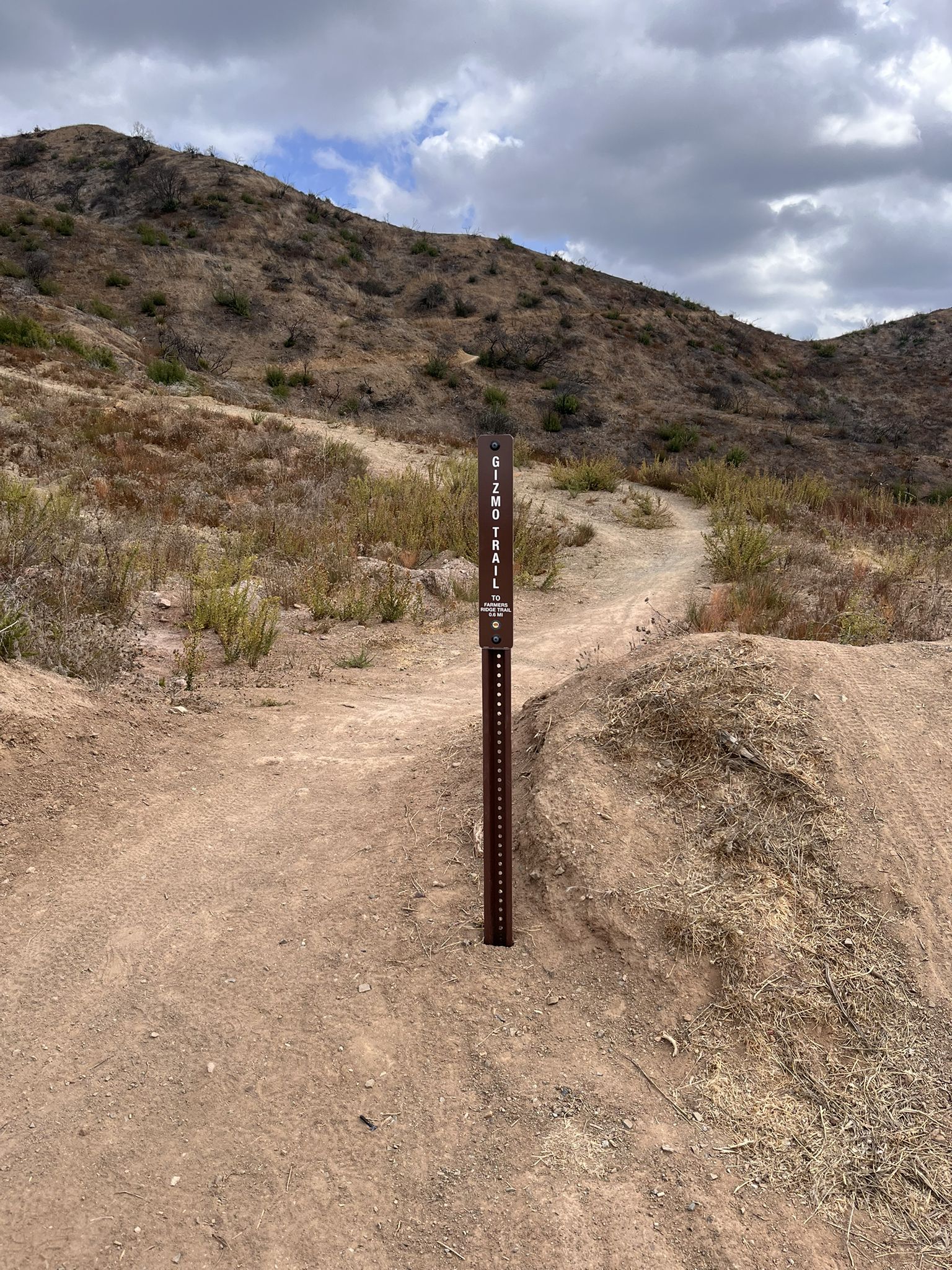 A brown trail marker stands on a dirt path through dry, rocky hills. - Mulholland Drive upper views – Dirt Mulholland loop from LA City Open Space