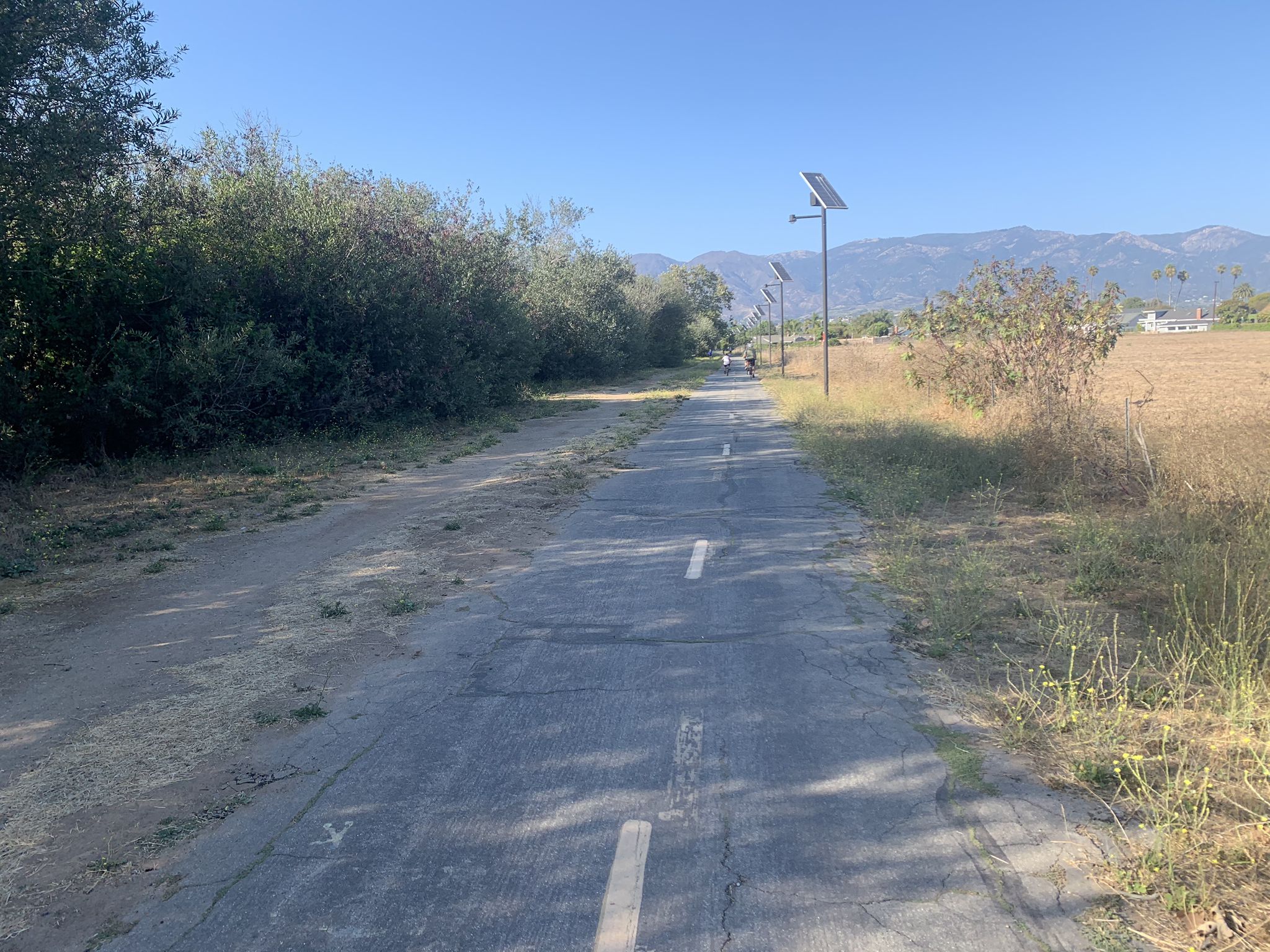 A paved path with solar lights, dry grass, and distant mountains. - Maria Ygnacio Bike Route – Atascadero Creek dirt trail loop from Goleta