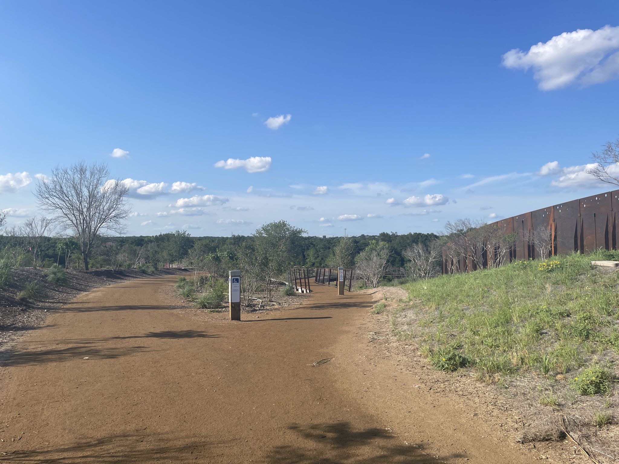 Sunny dirt path splits, leading to distant trees and a tall fence. - Salado Creek Greenway