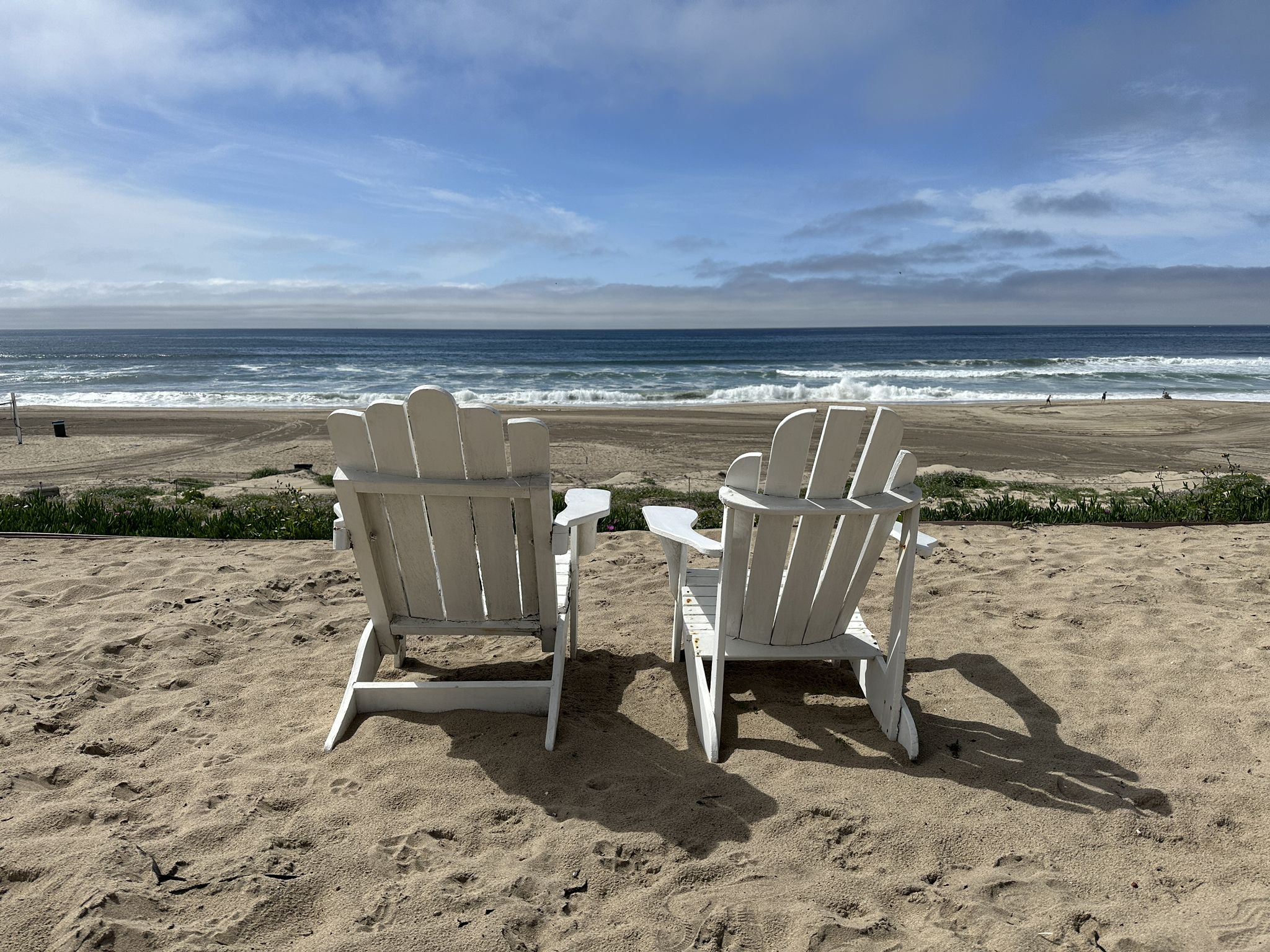 Two white Adirondack chairs on a sandy beach facing the ocean waves. - Surf Shack Beachside Café – Manhattan Beach loop from Manhattan Beach