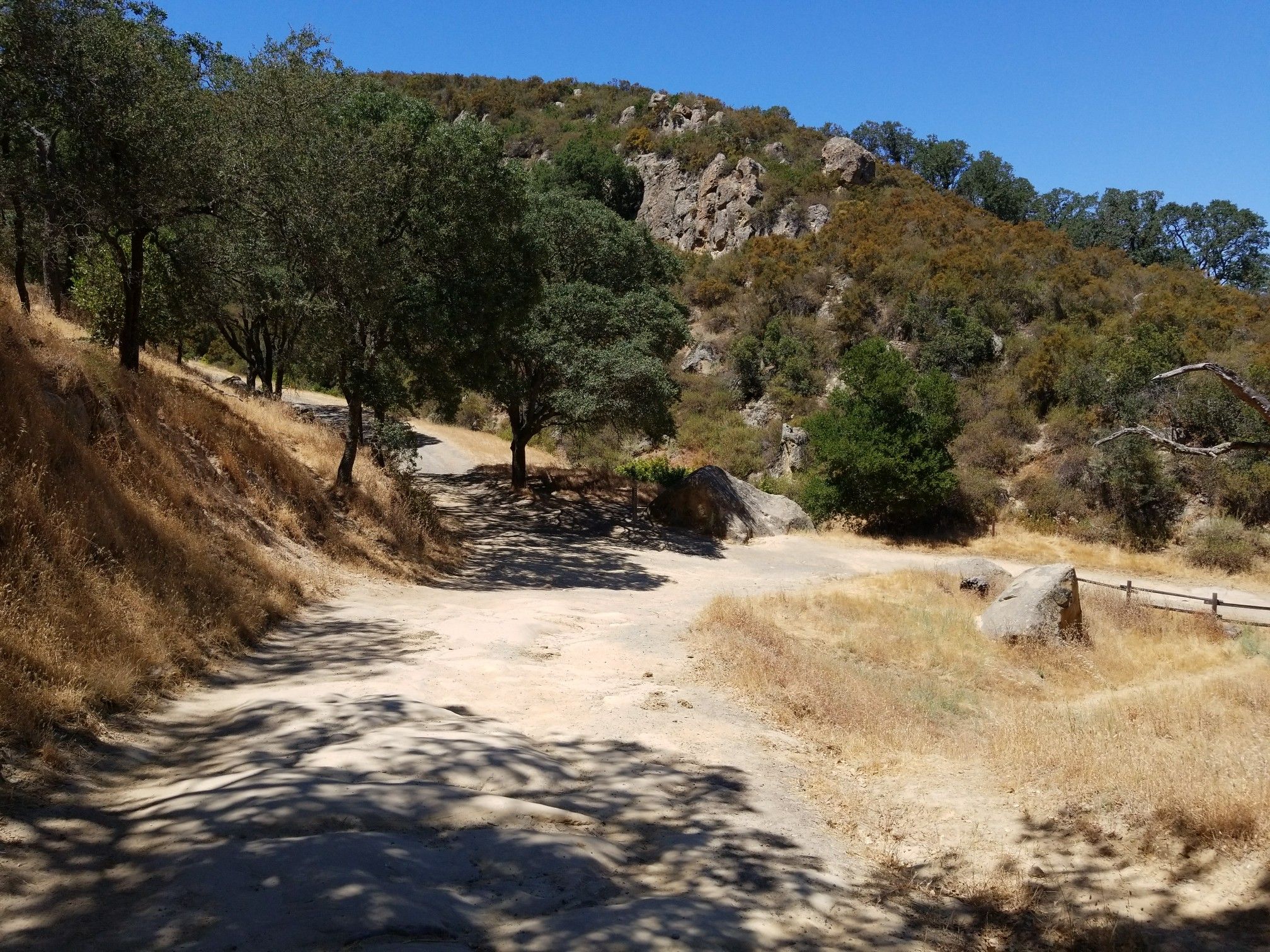 Dirt road through dry grass and trees, leading to rocky hills. - Stage Road Trail