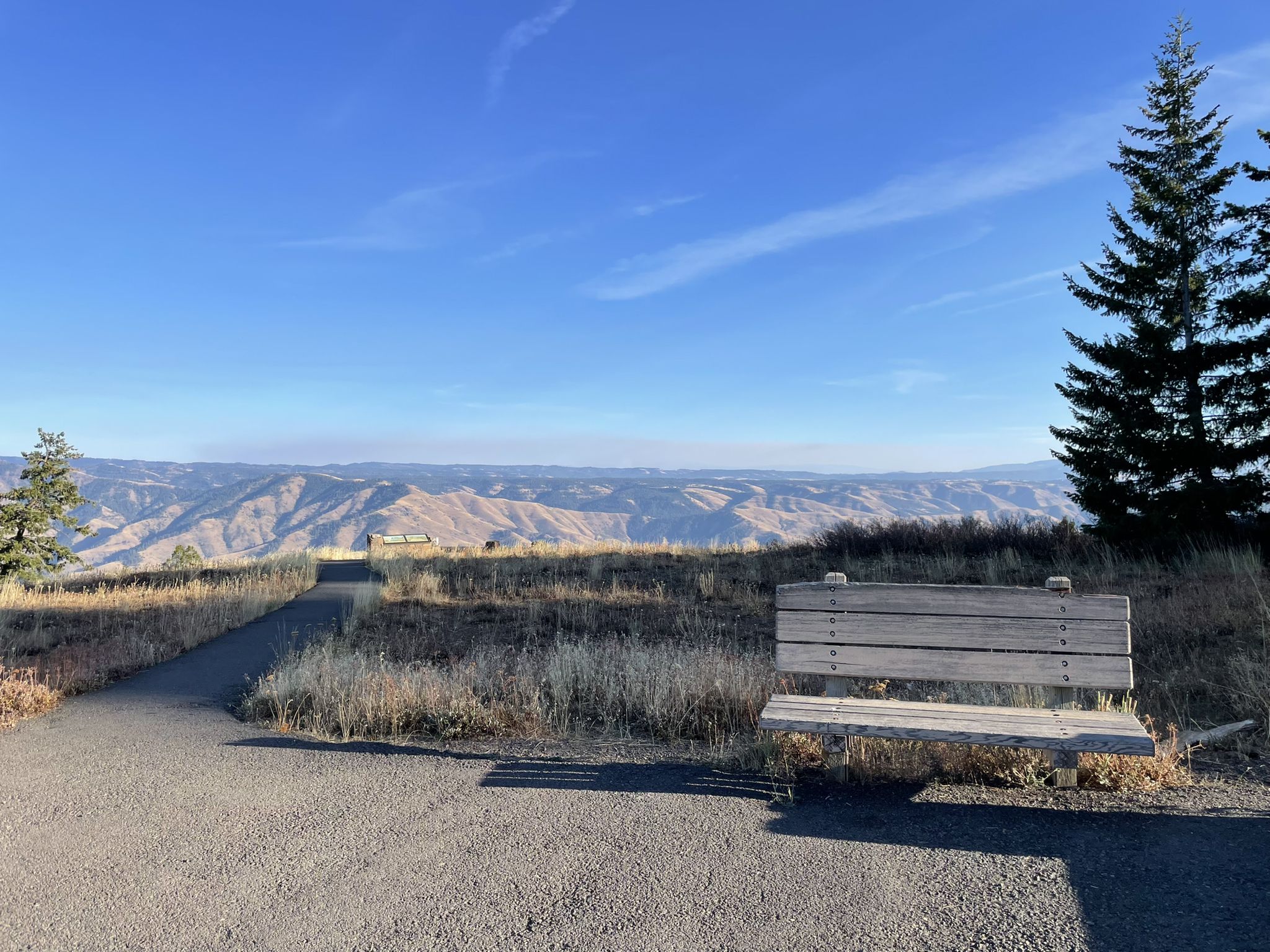 Wooden bench and paved path on a sunny hillside overlooking distant mountains. - Hells Canyon via Indian Crossing Campground loop